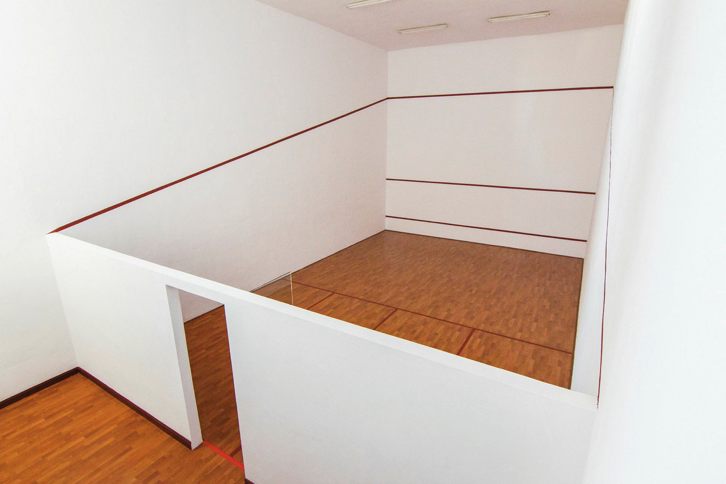 Sisätilojen squashkenttä, jossa valkoiset seinät ja puulattia. (Tekoälyn luoma teksti)