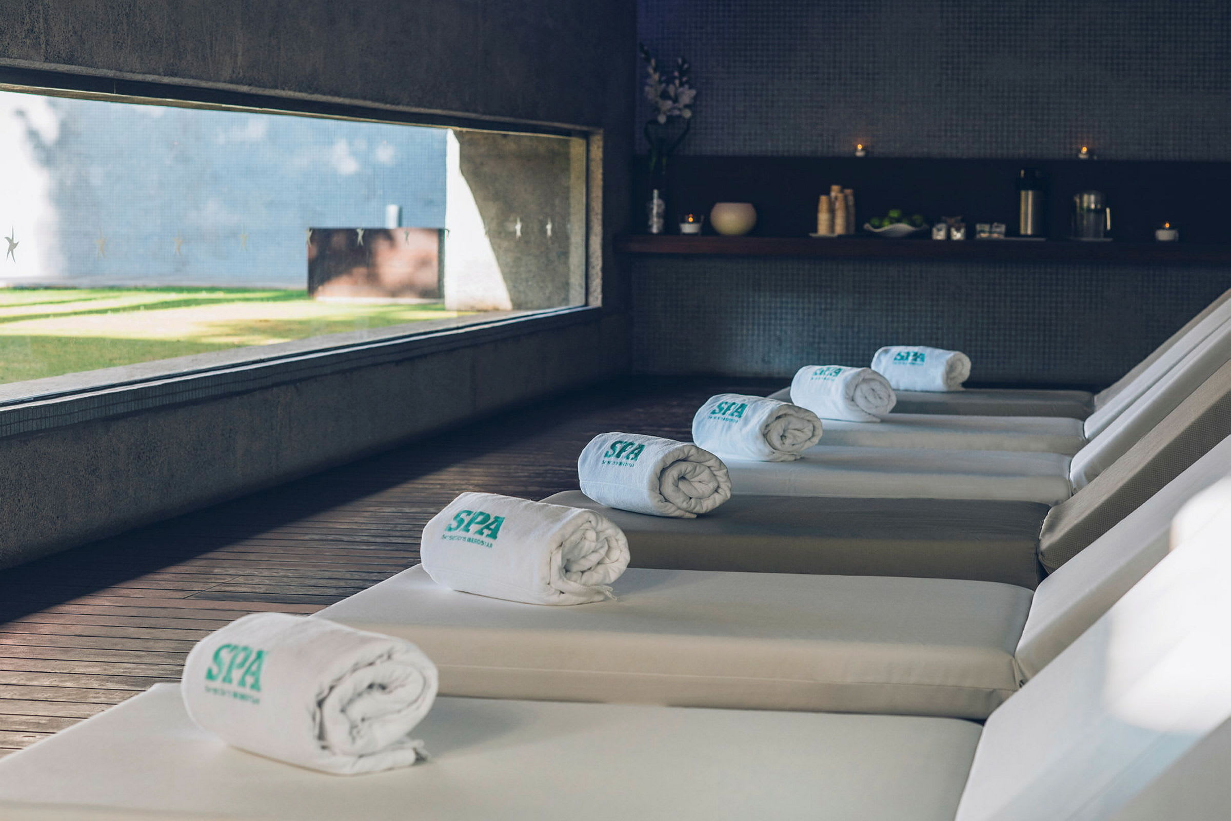 Aurinkotuoleja, joissa on valkoisia pyyhkeitä spa-ympäristössä, jossa on suuri ikkuna, josta avautuu näkymä nurmikentälle. (Tekoälyn luoma teksti)
