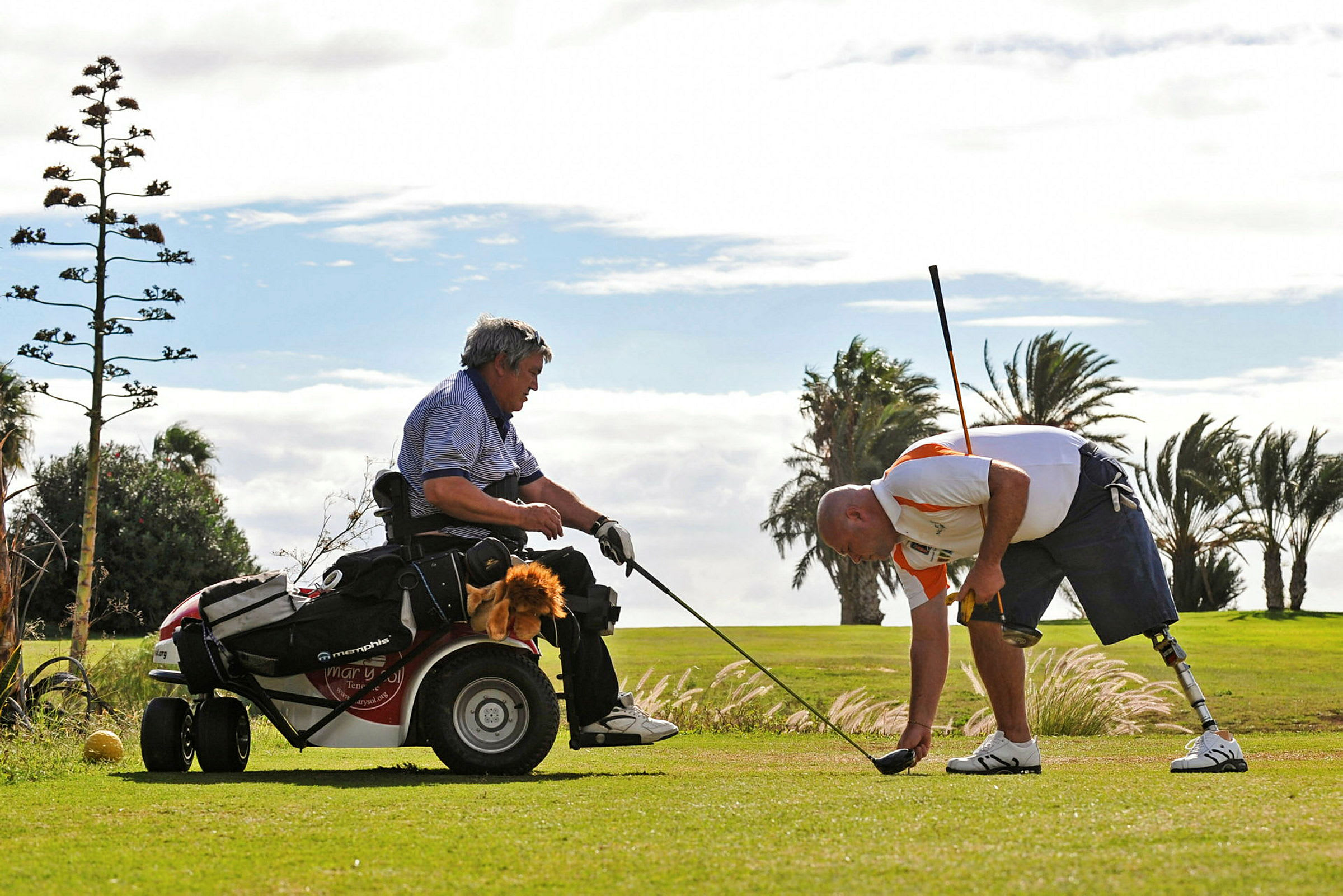 Kaksi henkilöä pelaa golfia, toinen istuu golfkärryssä ja toinen kumartuu nurmikolla golfmailan kanssa. (Tekoälyn luoma teksti)