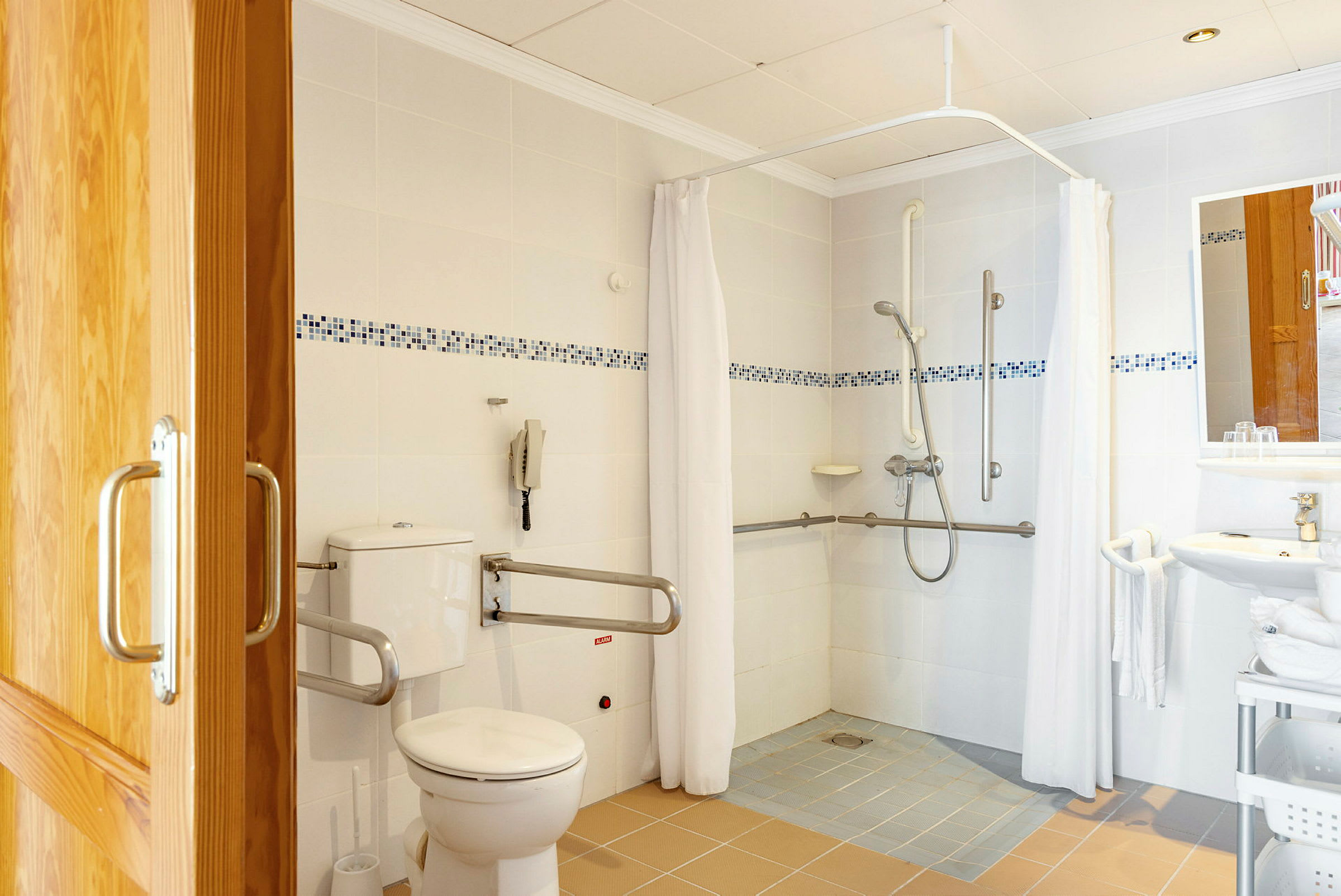 Kylpyhuone, jossa suihkutila, WC ja pesuallas varustettuna tukikahvoilla. (Tekoälyn luoma teksti)