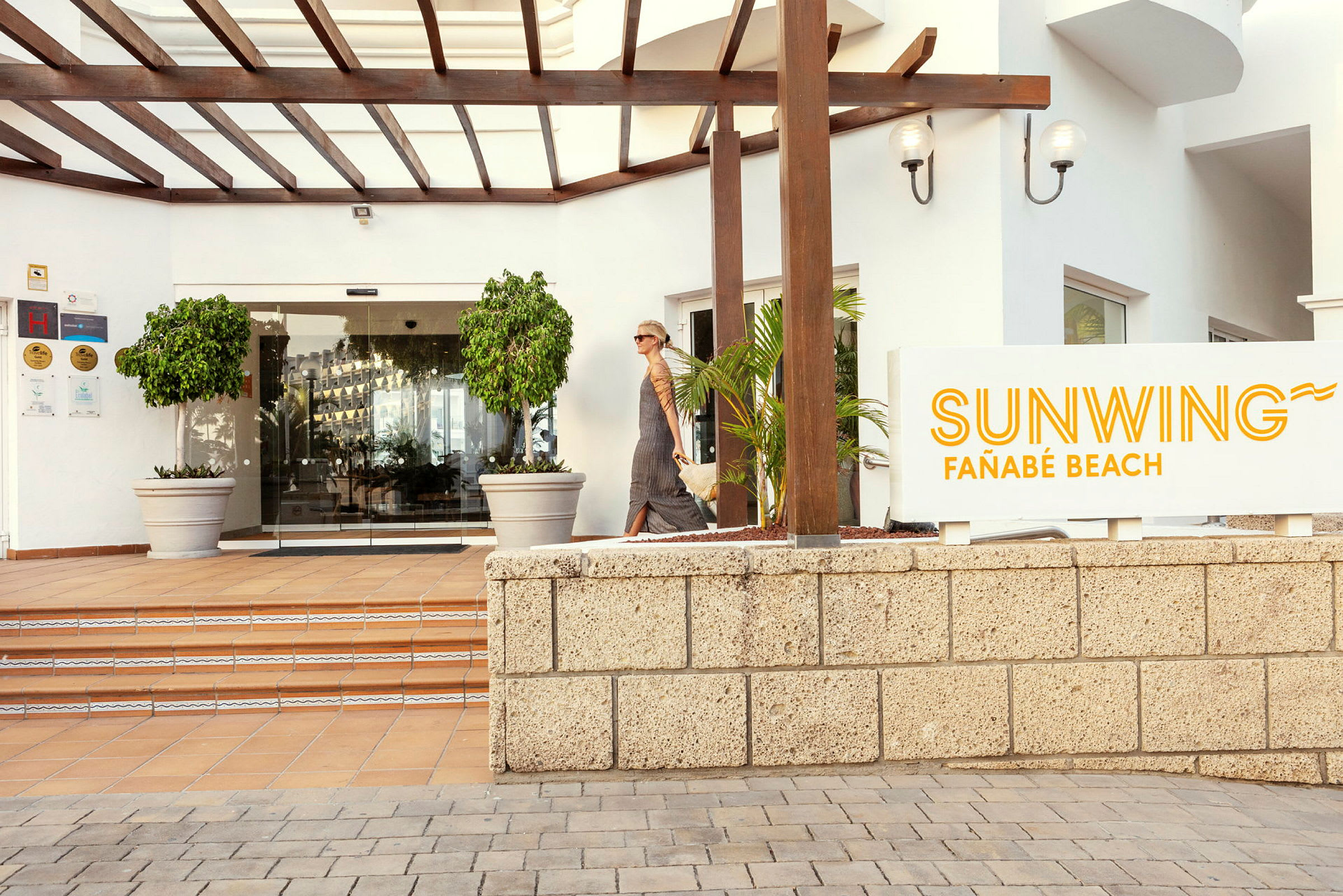Sunwing Fañabé Beachin sisäänkäynti kyltillä ja lasiovilla. (Tekoälyn luoma teksti)