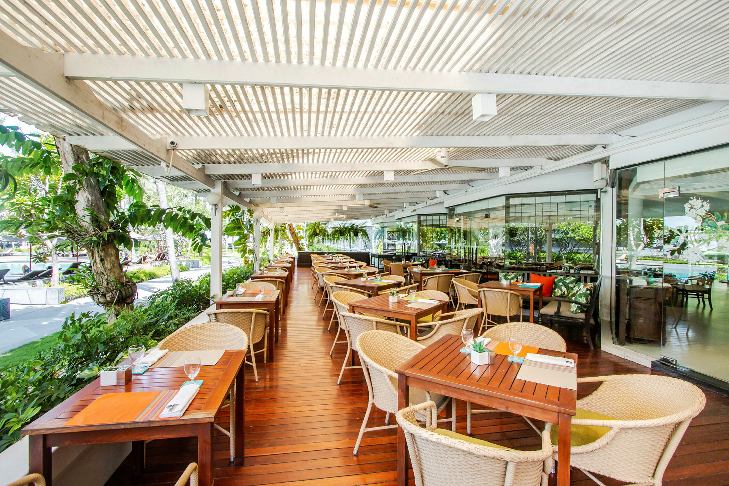 Ulkoterassiravintola, jossa puiset pöydät ja tuolit katetun pergolan alla. (Tekoälyn luoma teksti)