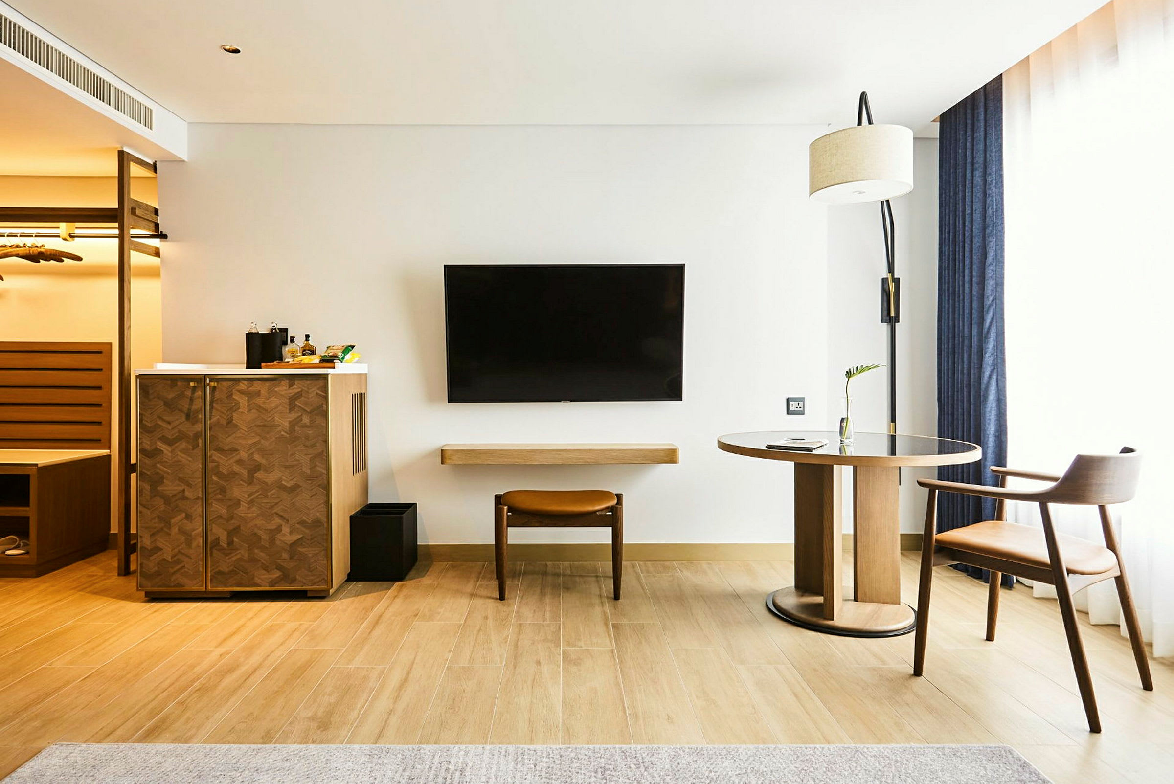 Hotellihuone, jossa on puukalusteita, seinälle asennettu televisio ja suuret verhotet ikkunat. (Tekoälyn luoma teksti)