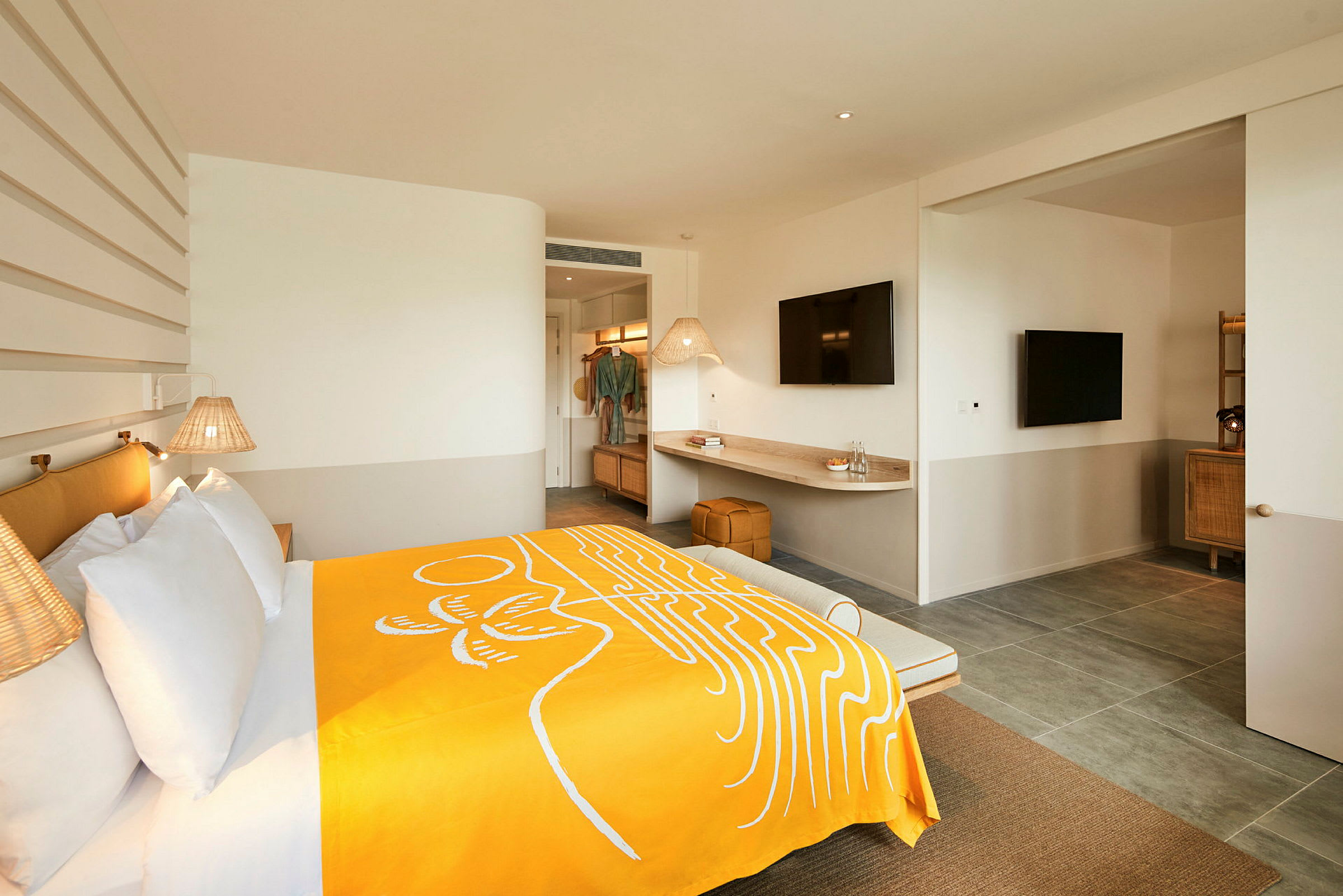 Moderni hotellihuone, jossa leveä sänky, keltainen peite, seinävalaisimet ja pöytäpinta, jonka yläpuolella on televisio. (Tekoälyn luoma teksti)