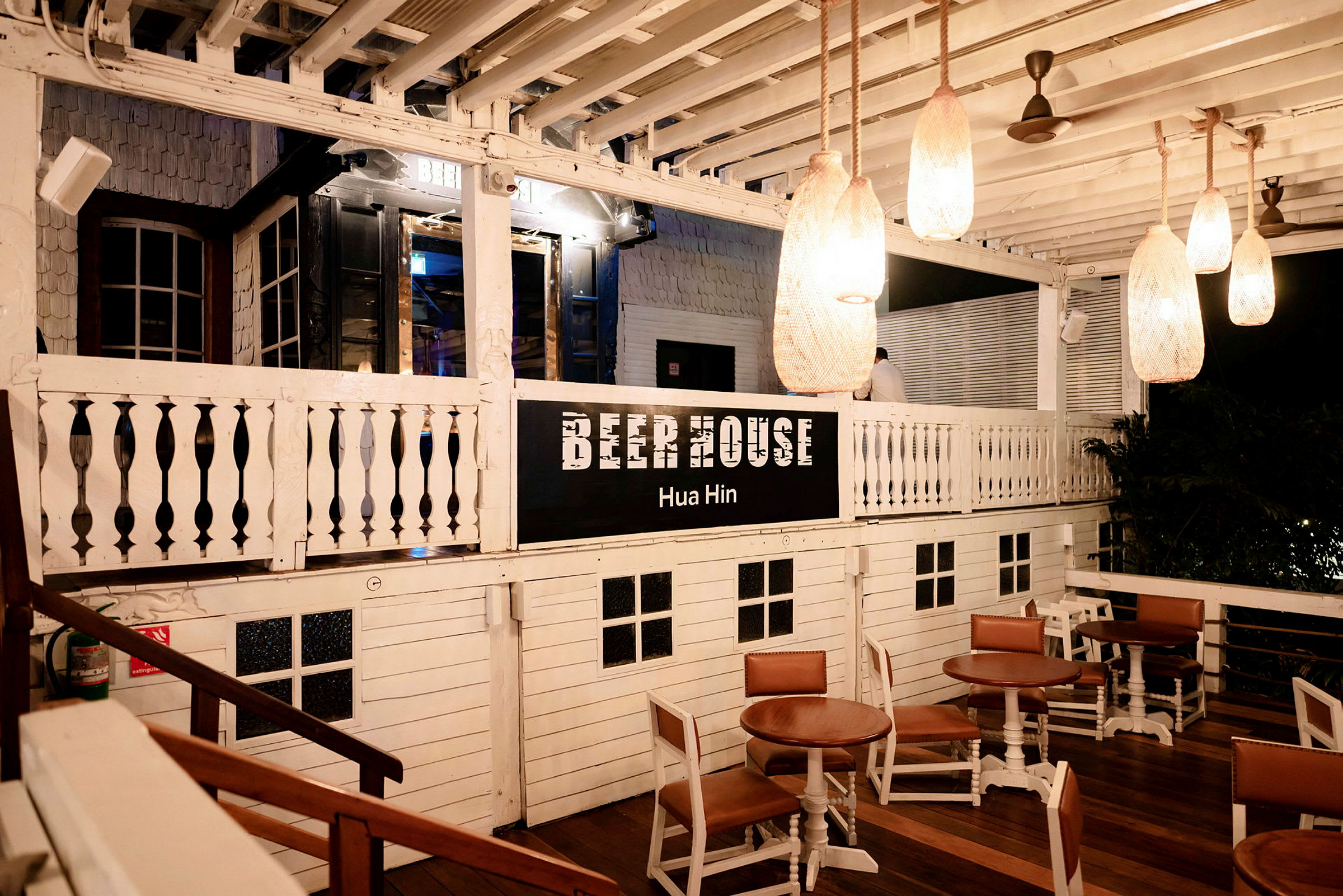 Puinen rakennus, jossa lukee 'Beer House Hua Hin'. Ulkoterassilla on pöytiä ja tuoleja. (Tekoälyn luoma teksti)