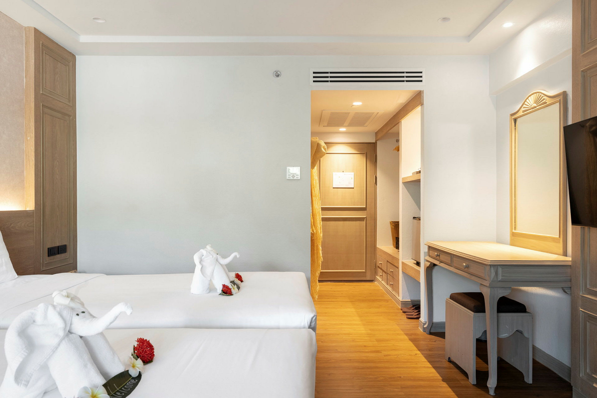 Hotellihuone, jossa kaksi erillistä vuodetta ja pyyhehahmoja koristeina. Sisustus sisältää työpöydän ja vaatekaapin sisäänkäynnin. (Tekoälyn luoma teksti)