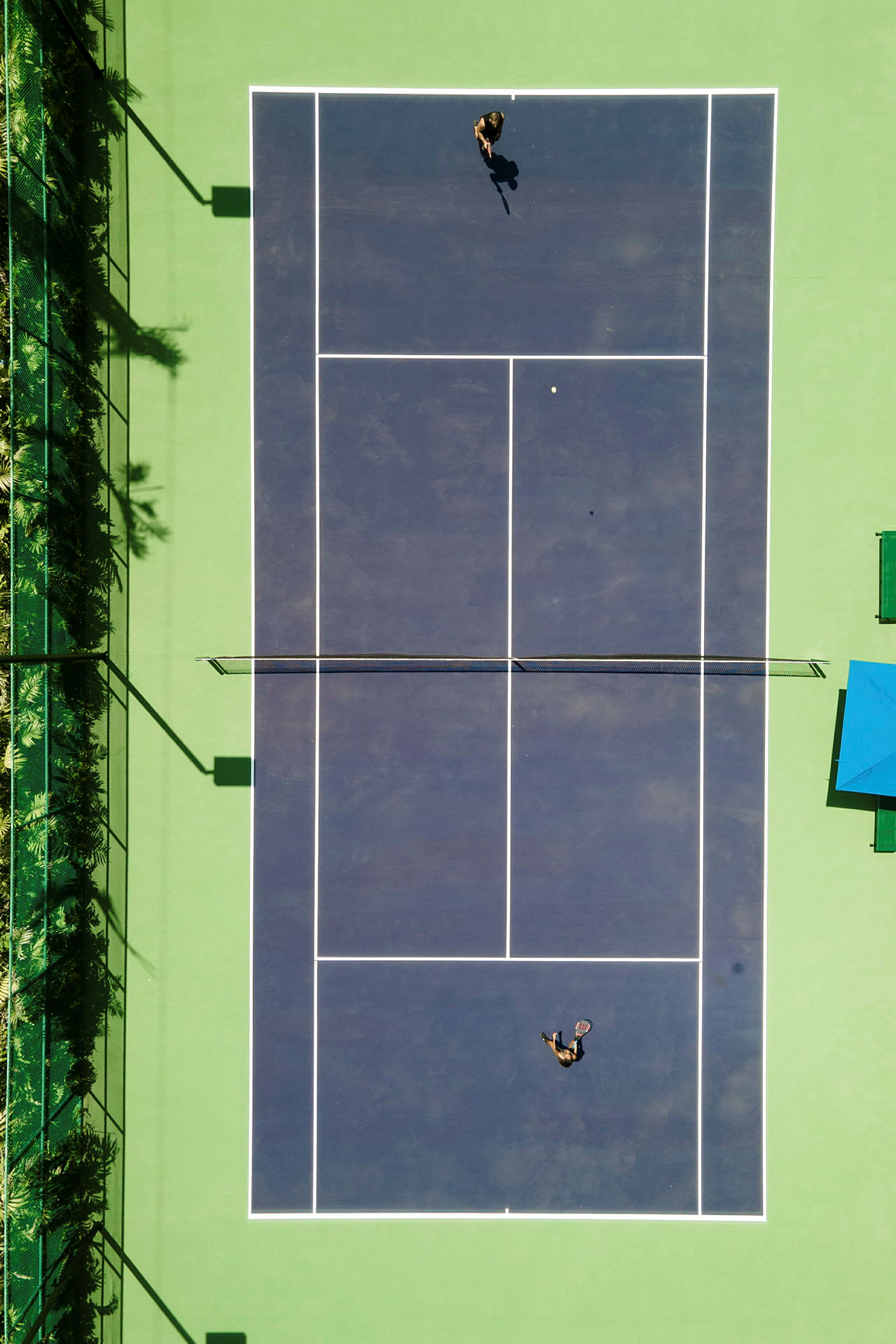 Ilmakuva tenniskentästä, jossa kaksi henkilöä pelaa tennistä. (Tekoälyn luoma teksti)