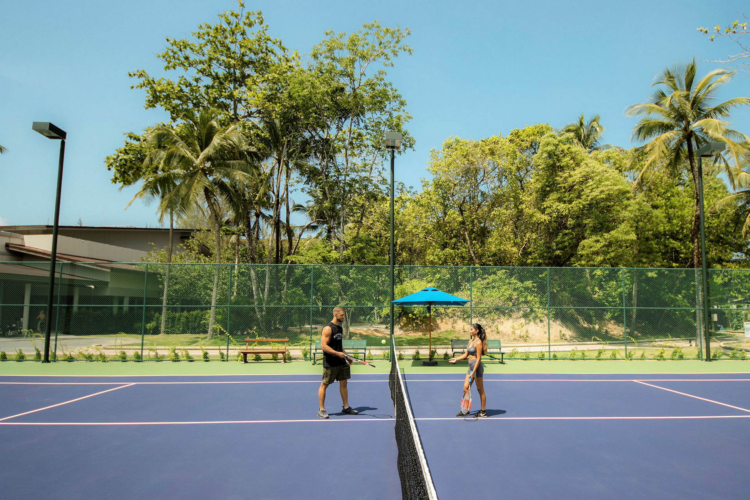Kaksi henkilöä pelaa tennistä ulkokentällä, ympäröivät puut. (Tekoälyn luoma teksti)