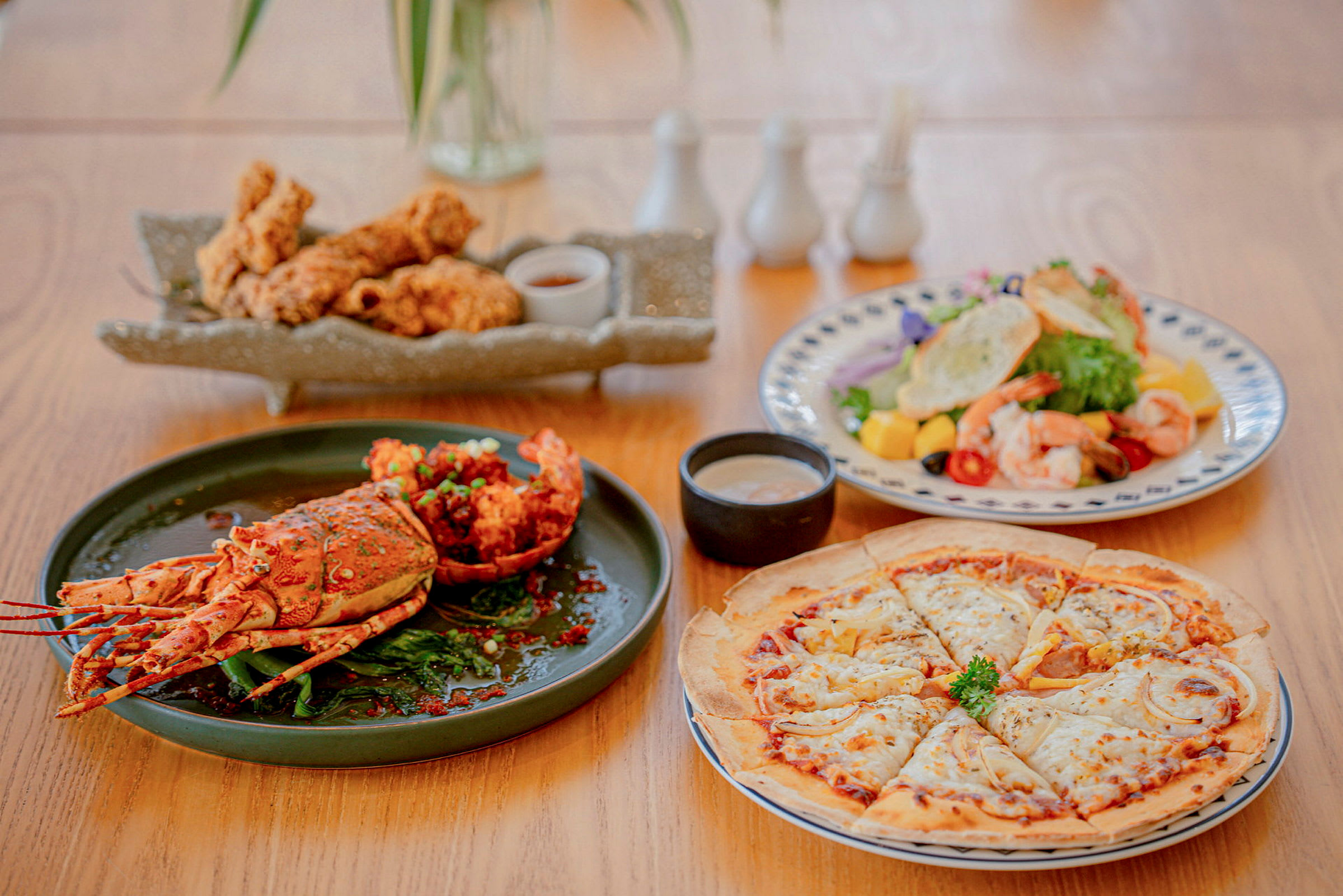 Ruokapöytä, jossa on aterioita, kuten hummeri, paistettuja kananpaloja, katkarapu- ja trooppinen hedelmäsalaatti sekä pizza. (Tekoälyn luoma teksti)