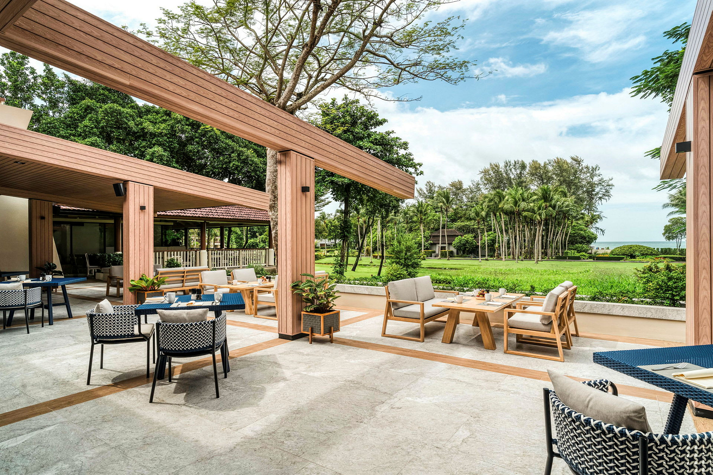 Kuva ulkoterassista, jossa on istumapaikkoja, pöytiä ja vihreää taustalla. (Tekoälyn luoma teksti)