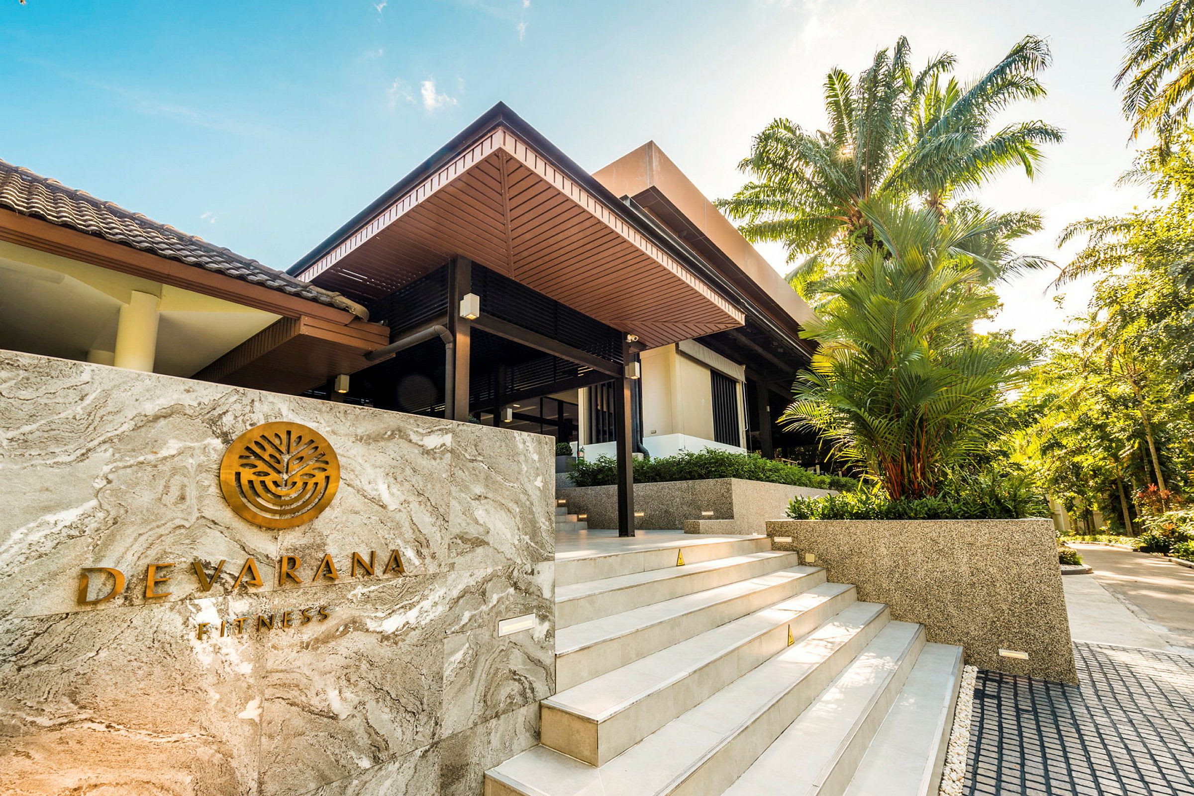 Kuva modernista rakennuksesta puuyksityiskohdilla, jota ympäröi vihreys. Etualalla näkyy kyltti, jossa lukee "Devarana Fitness". (Tekoälyn luoma teksti)