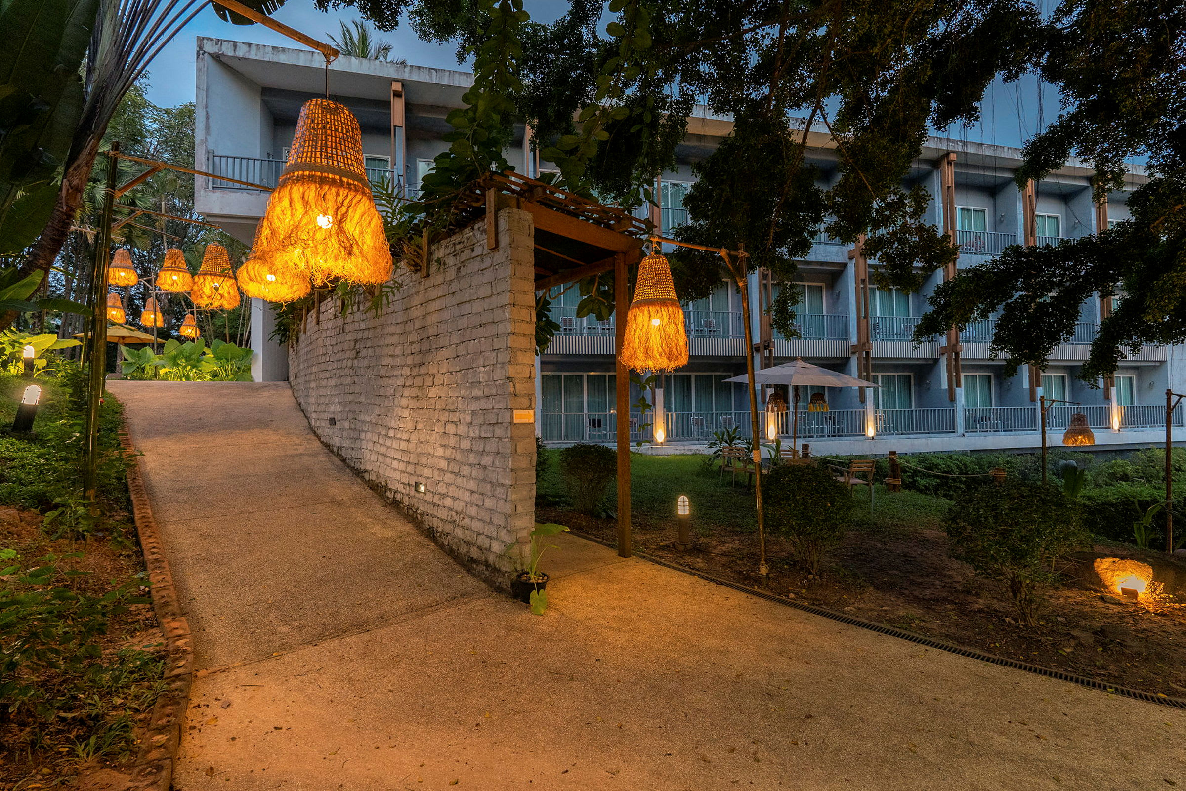 Polku, jota reunustavat kasvit ja valaisimet ja joka johtaa parvekkeilla varustettuun rakennukseen. (Tekoälyn luoma teksti)
