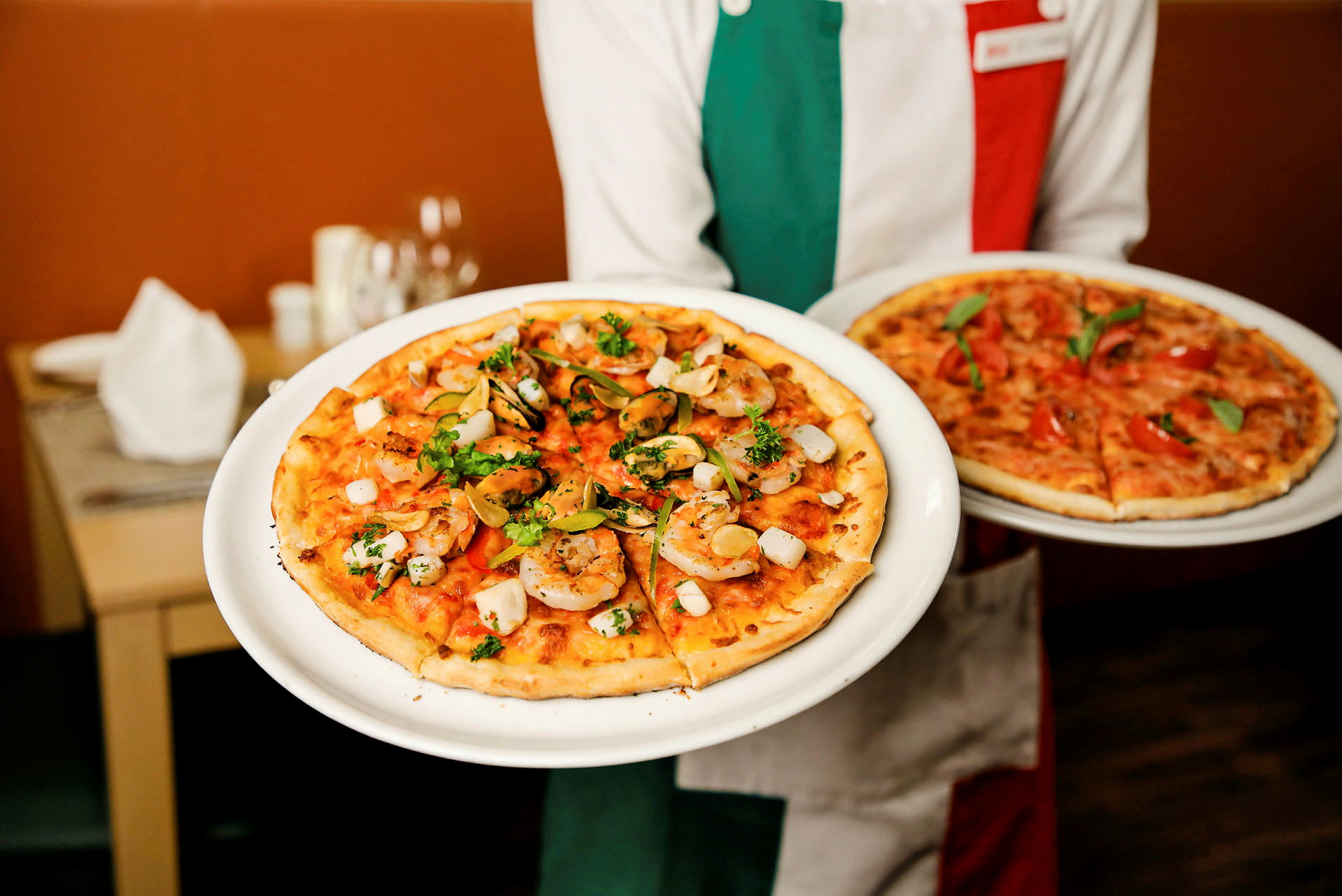Henkilö pitää kahta lautasellista pizzoja, joista toisessa on katkarapuja ja yrttejä täytteenä. (Tekoälyn luoma teksti)