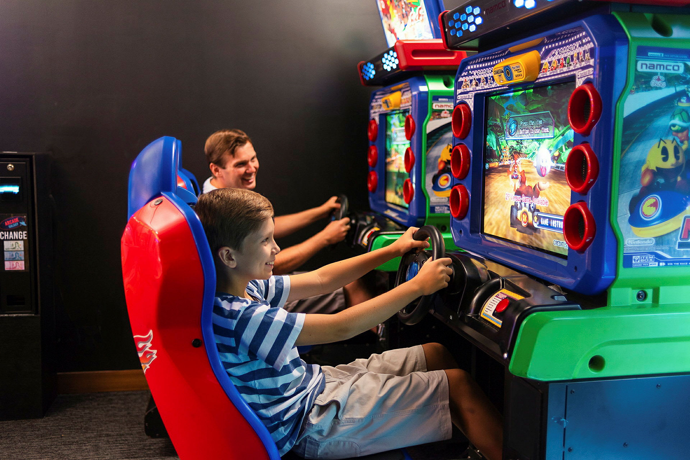 Kaksi henkilöä pelaa arcade-autoilupeliä. (Tekoälyn luoma teksti)