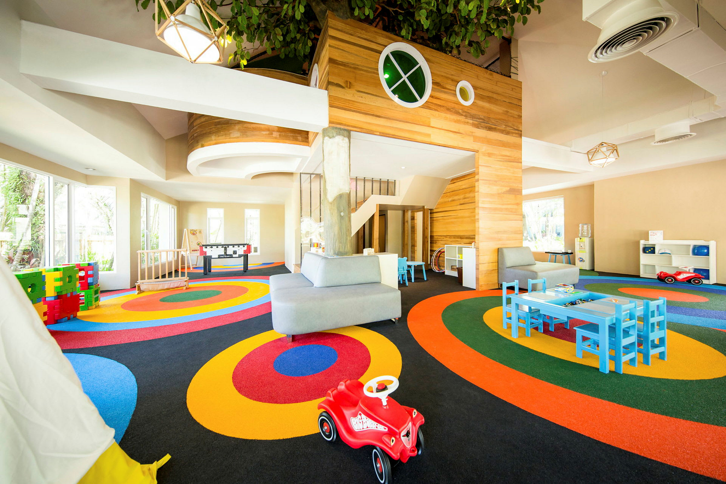 Värikäs leikkialue, jossa on lasten kokoisia huonekaluja ja sisäleikkipaikka. (Tekoälyn luoma teksti)