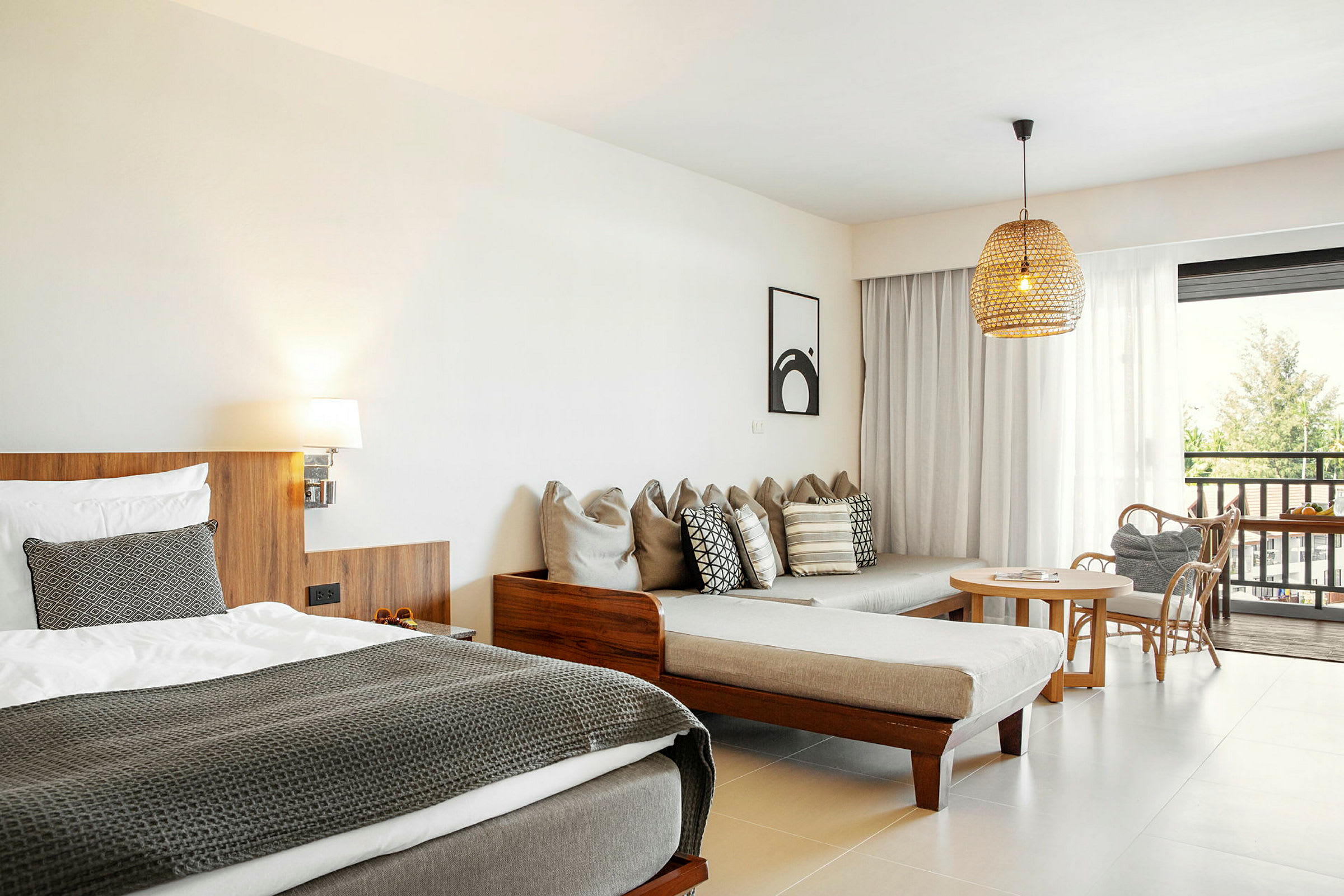 Hotellihuone, jossa on sänky, sohva, tyynyjä, pöytä ja tuolit sekä näkymä ulos lasiovista. (Tekoälyn luoma teksti)