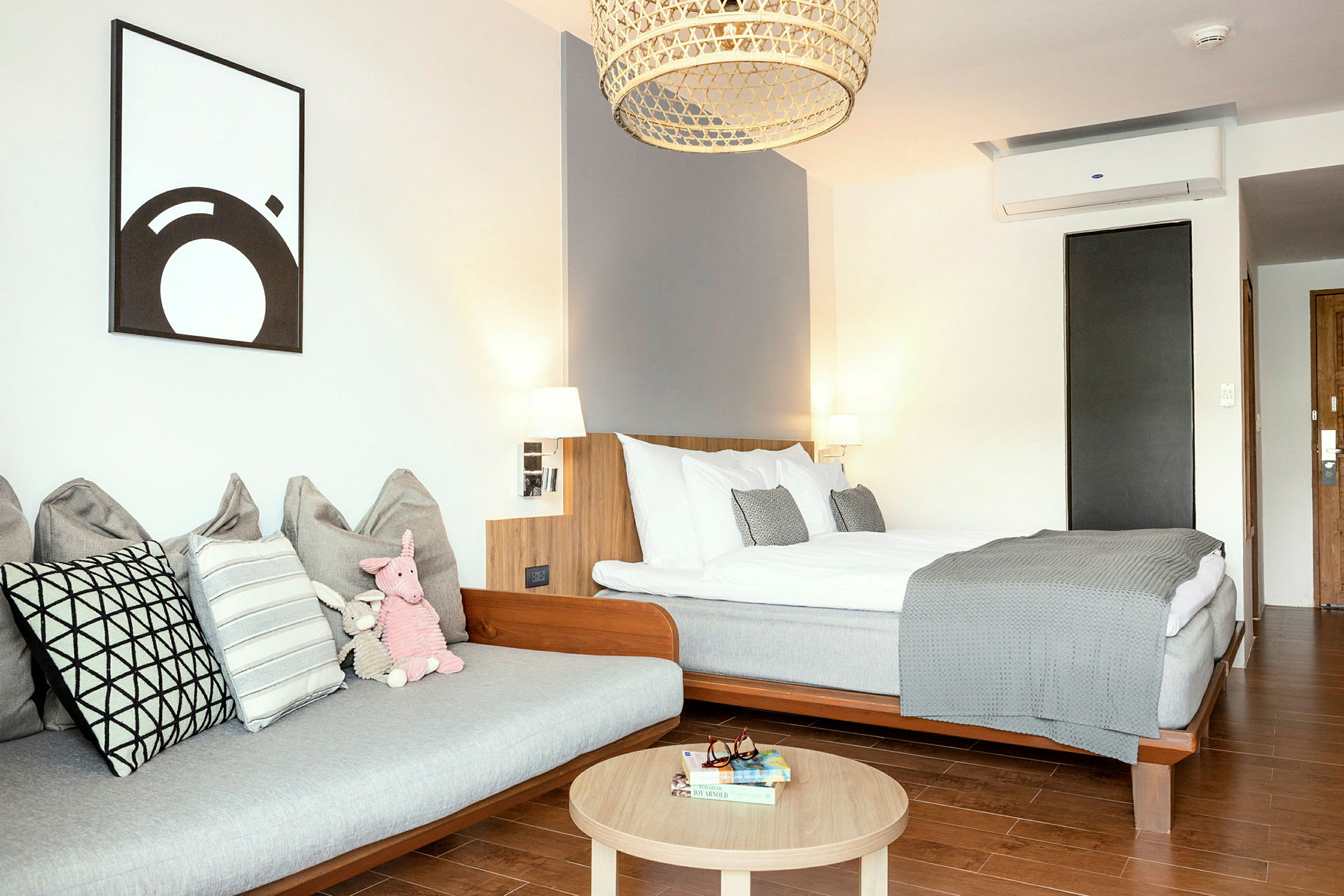 Moderni hotellihuone, jossa sänky, sohva ja puupöytä. (Tekoälyn luoma teksti)