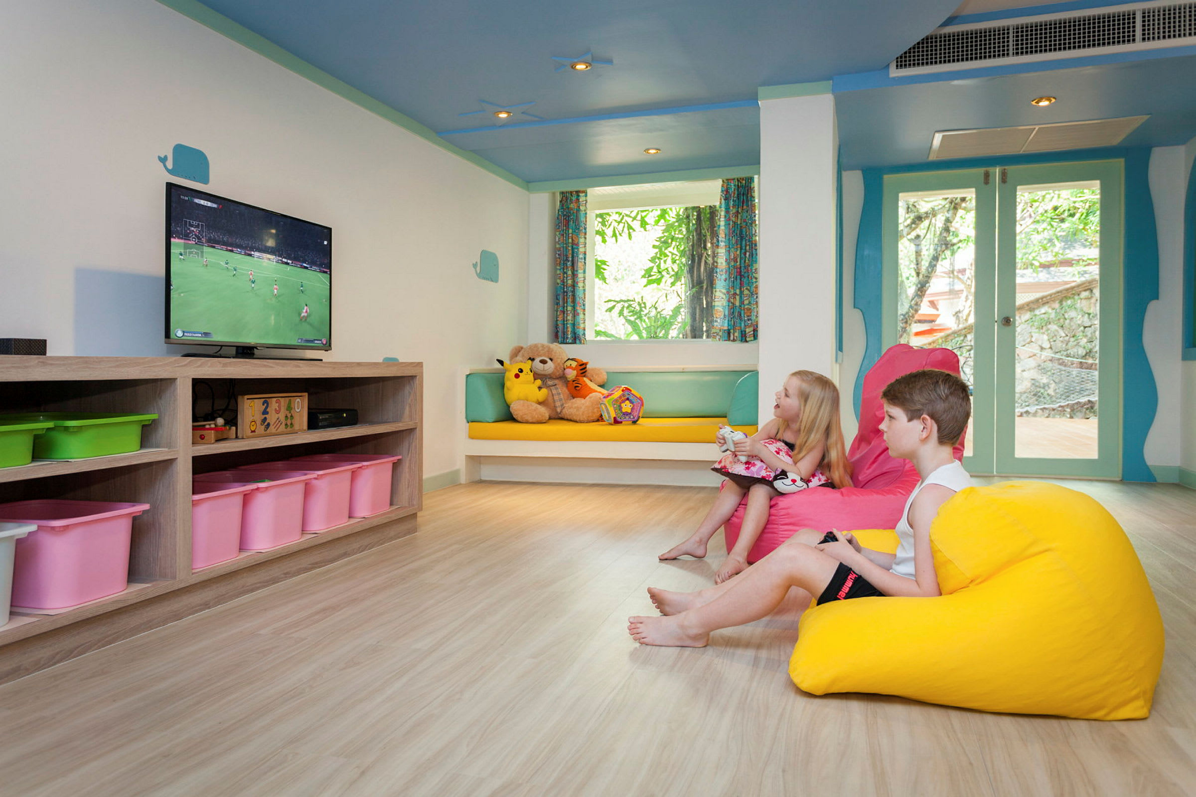 Lastenhuone, jossa on värikkäitä säkkituoleja, leluja hyllyssä ja televisio seinällä. (Tekoälyn luoma teksti)