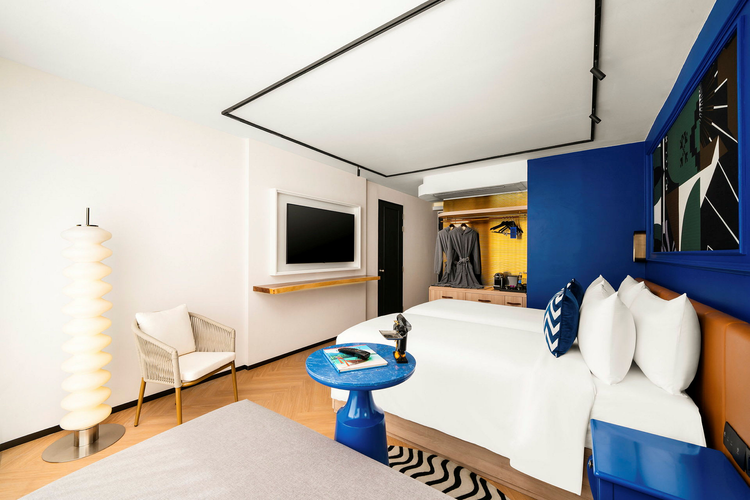 Moderni hotellihuone, jossa on suuri sänky, koristeellinen sisustus ja nojatuoli ainutlaatuisen lattiavalaisimen vieressä. (Tekoälyn luoma teksti)