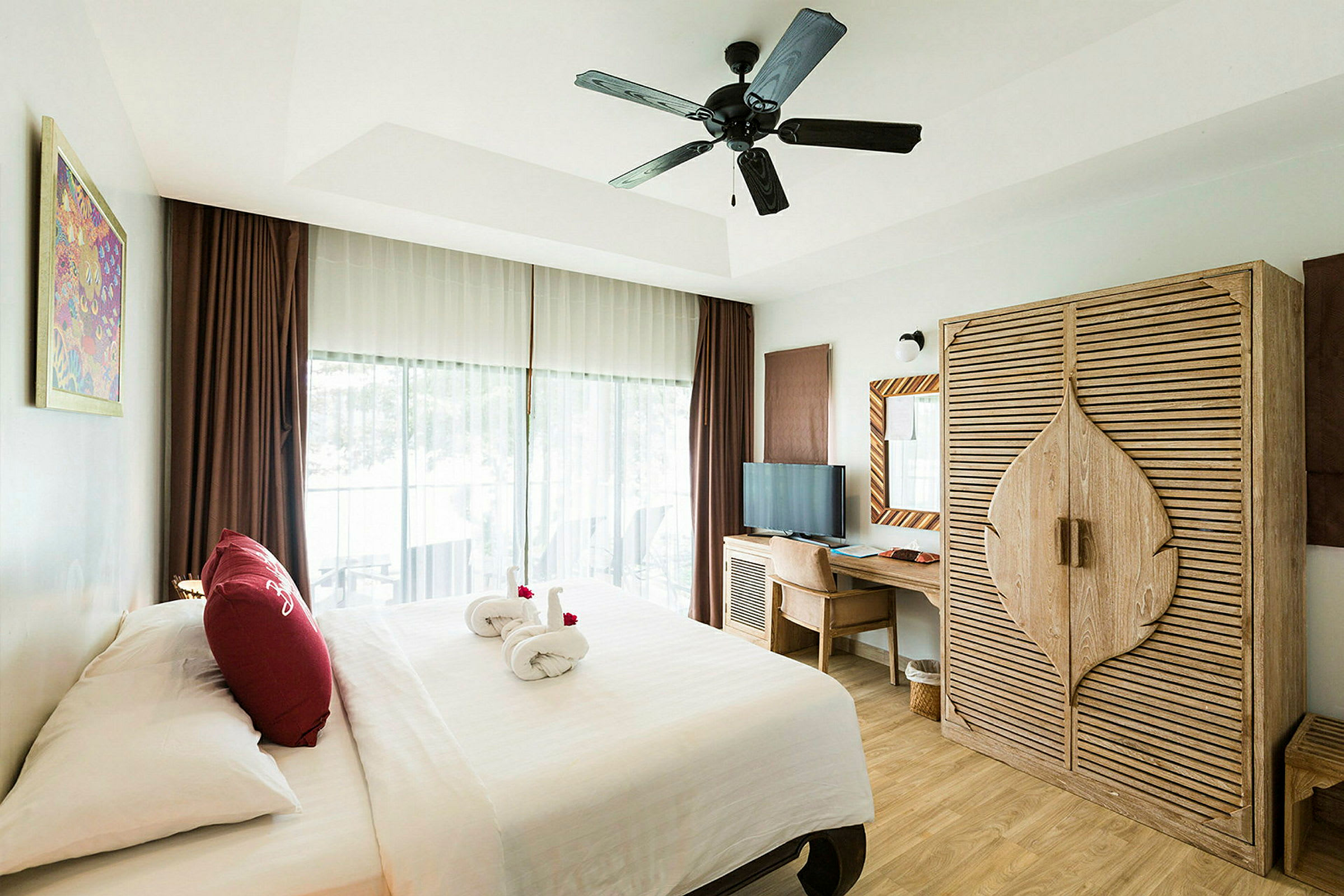 Hotellihuone, jossa on parivuode, puinen vaatekaappi, kirjoituspöytä ja tuoli sekä kattotuuletin. Ikkunasta, jossa on verhot, näkyy parveke. (Tekoälyn luoma teksti)