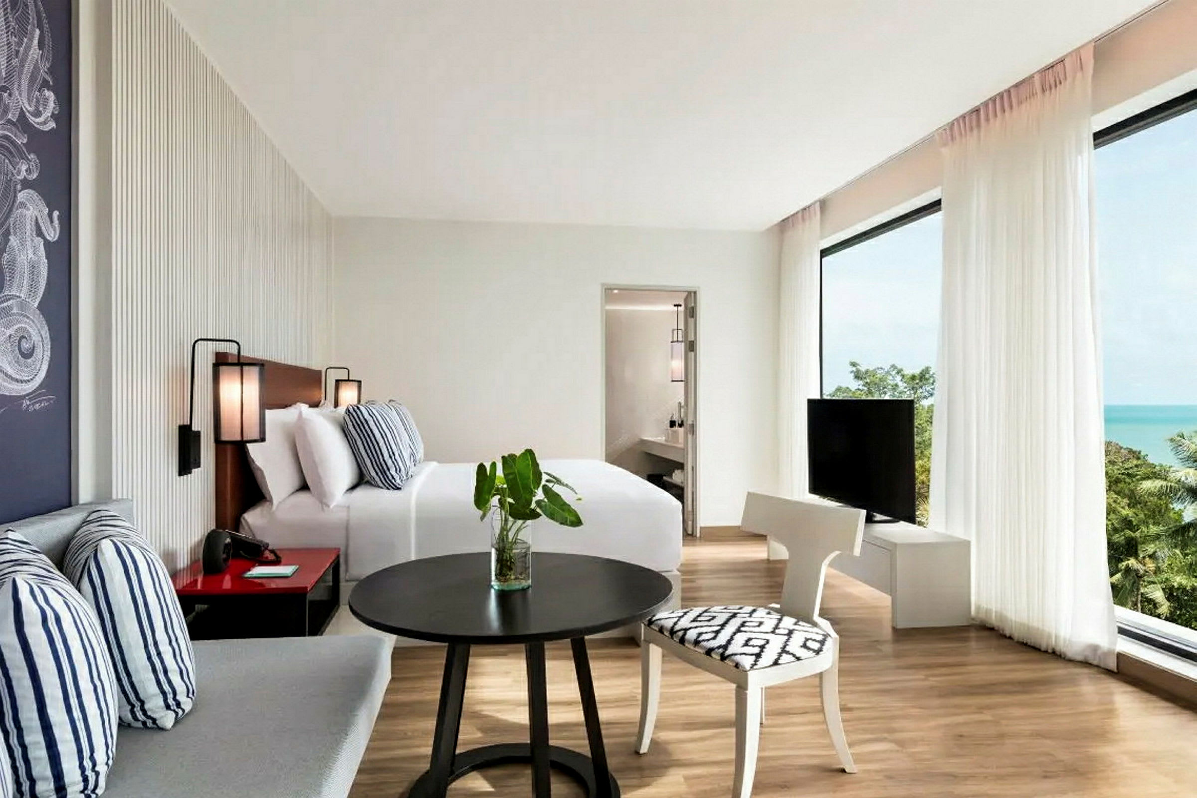 Valoisa hotellihuone, jossa sänky, istuma-alue, televisio ja näkymä merelle. (Tekoälyn luoma teksti)