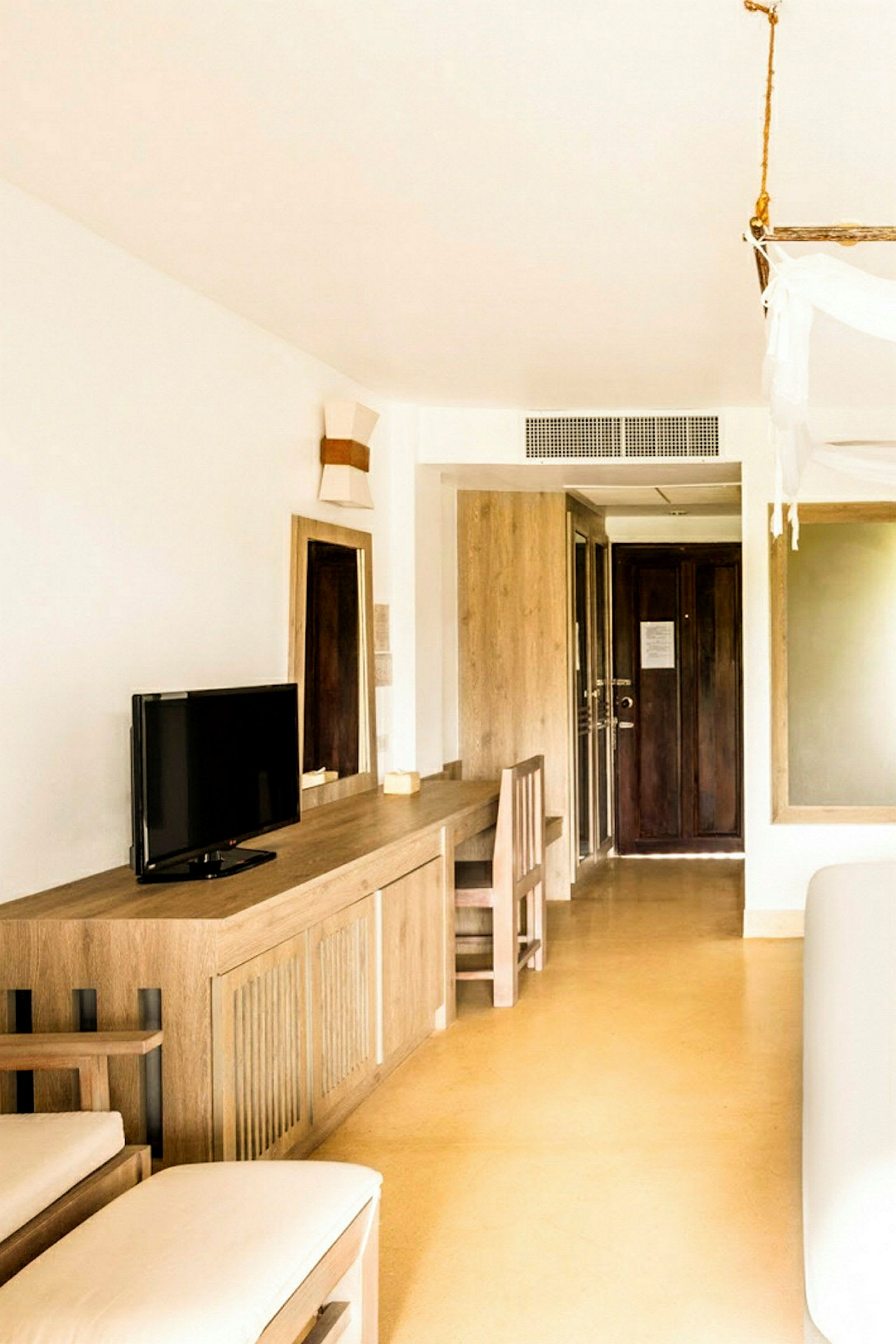 Hotellihuone, jossa on minimalistinen sisustus, mukaan lukien kirjoituspöytä, tuoli ja pieni TV. (Tekoälyn luoma teksti)