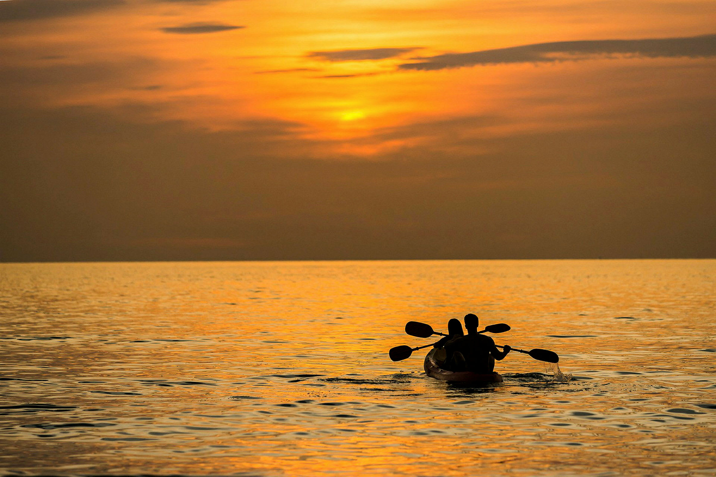 Kaksi henkilöä meloo kajakilla tyynellä merellä oranssin auringonlaskun alla. (Tekoälyn luoma teksti)