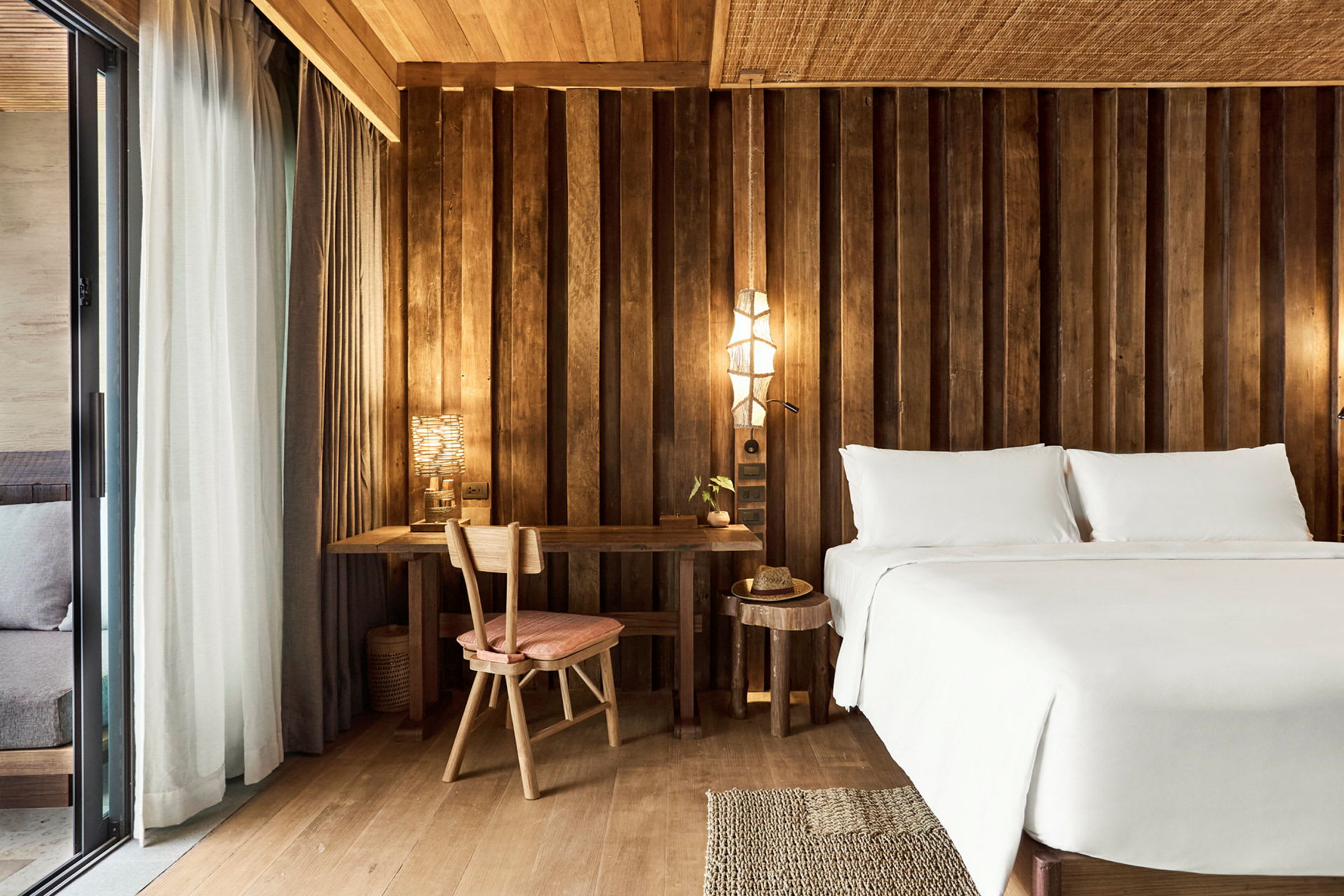 Hotellihuone, jossa on sänky, työpöytä ja tuoli, huoneessa puupaneelit. (Tekoälyn luoma teksti)