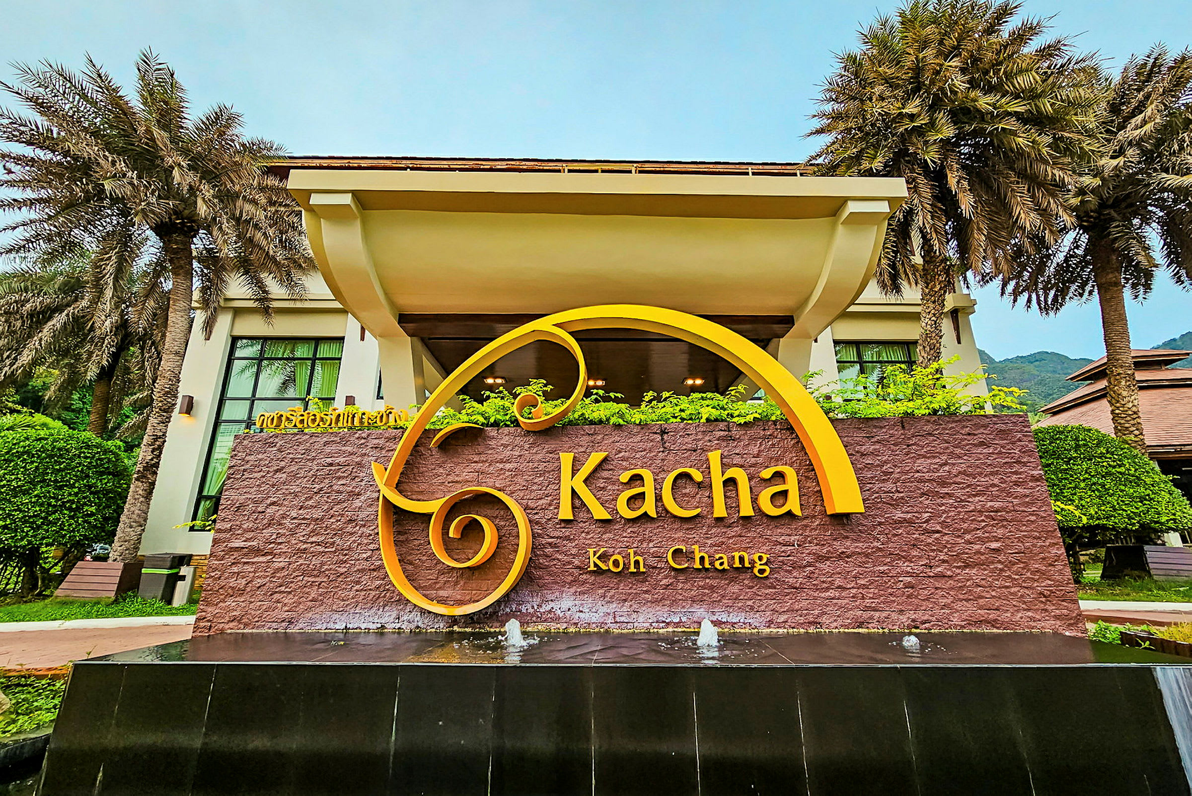 'Kacha Koh Chang' -kyltti rakennuksen edessä, jota ympäröivät kasvit ja palmut. (Tekoälyn luoma teksti)