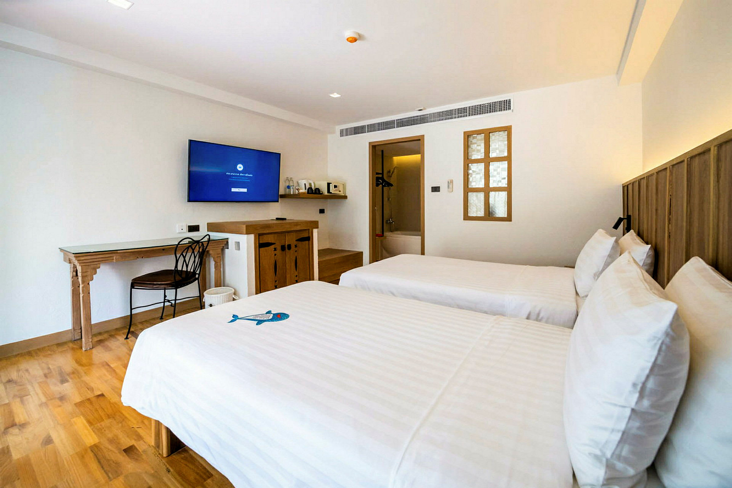 Hotellihuone jossa kaksi erillistä sänkyä, seinällä televisio ja puisia huonekaluja. (Tekoälyn luoma teksti)