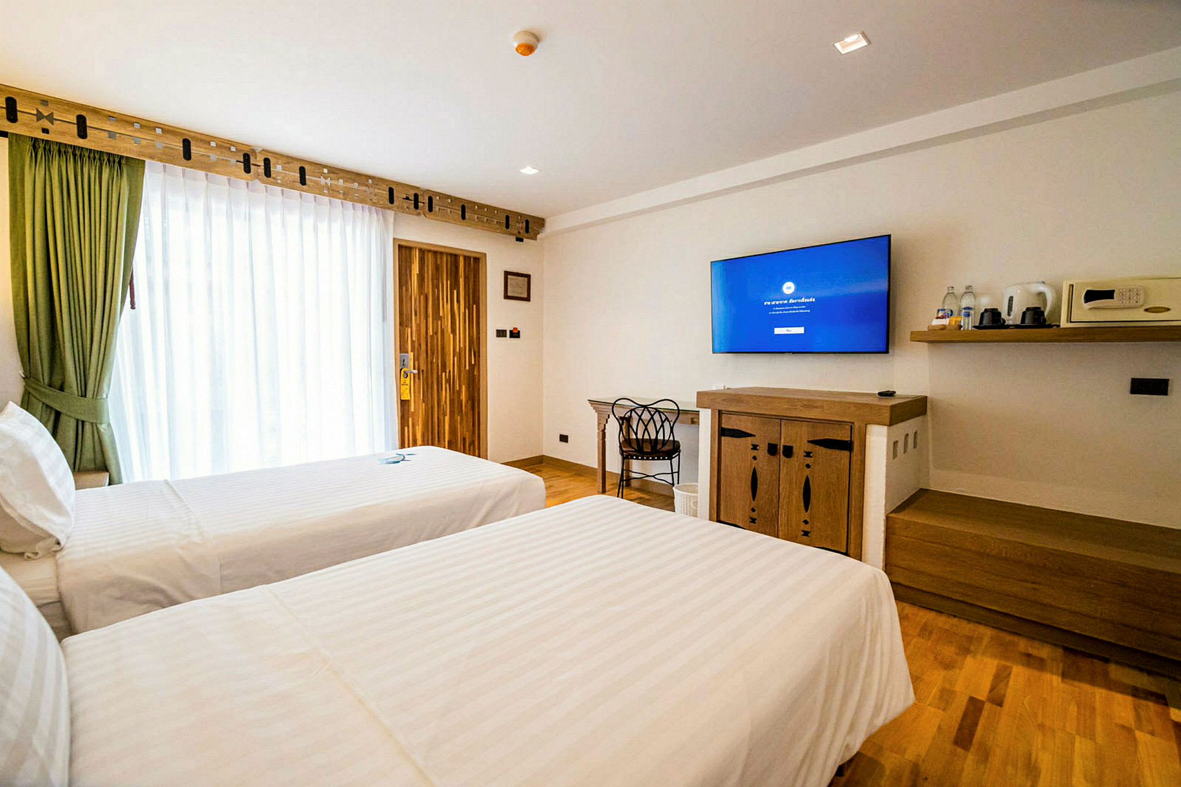 Hotellihuone, jossa kaksi yhden hengen vuodetta, seinällä televisio ja säilytyshylly. (Tekoälyn luoma teksti)