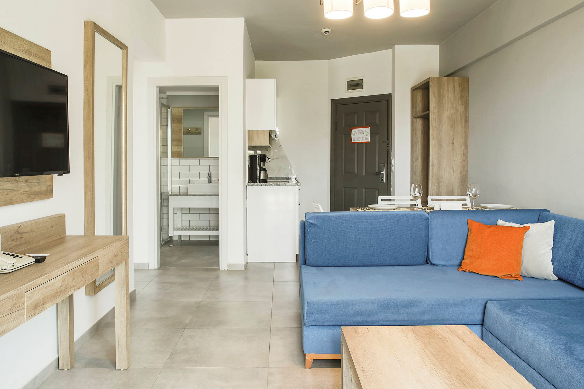 Hotellihuone, jossa on sininen sohva, kirjoituspöytä, televisio, keittiö ja kylpyhuone. (Tekoälyn luoma teksti)