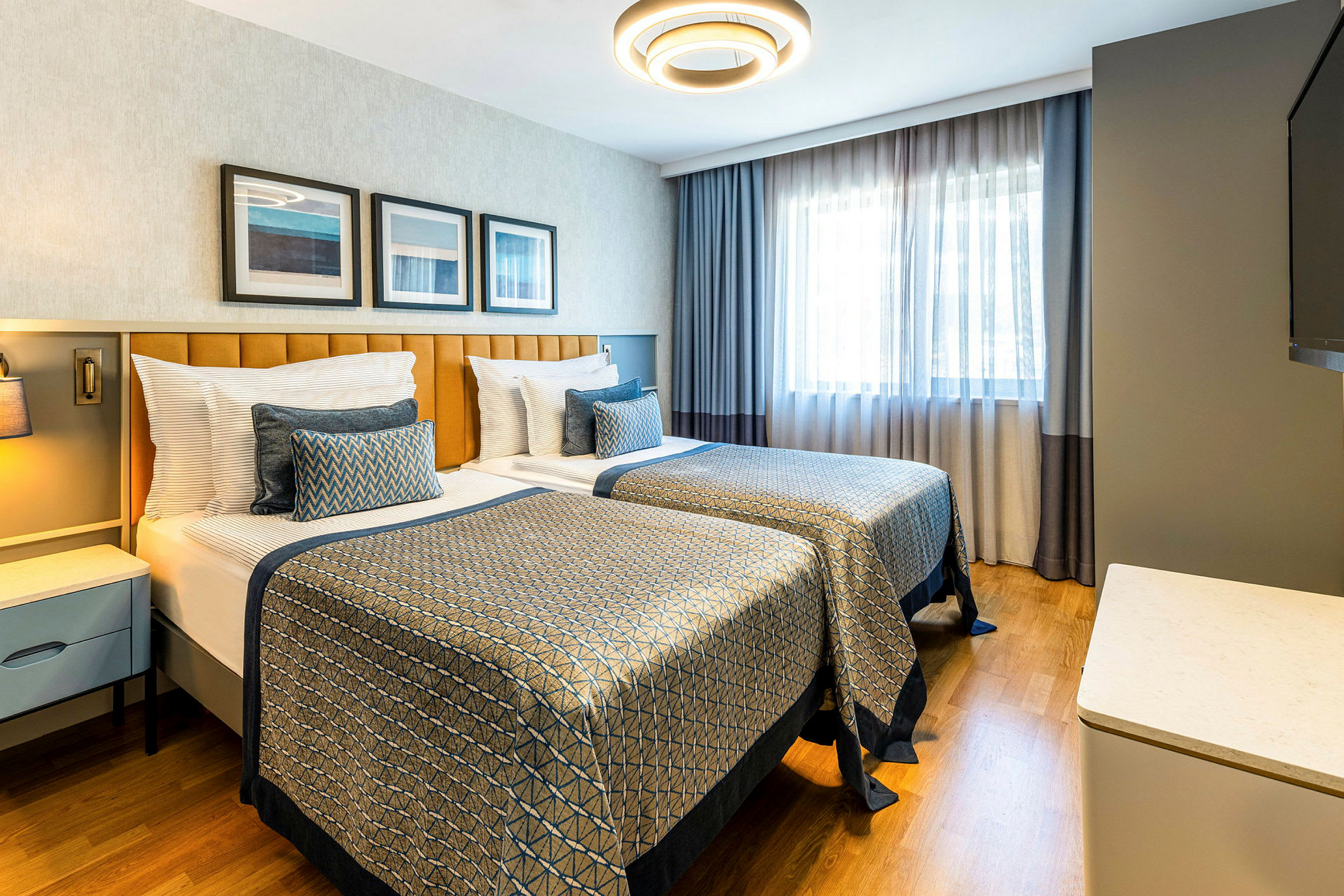 Hotellihuone, jossa on kaksi yhden hengen vuodetta, moderni sisustus ja luonnonvaloa ikkunasta. (Tekoälyn luoma teksti)