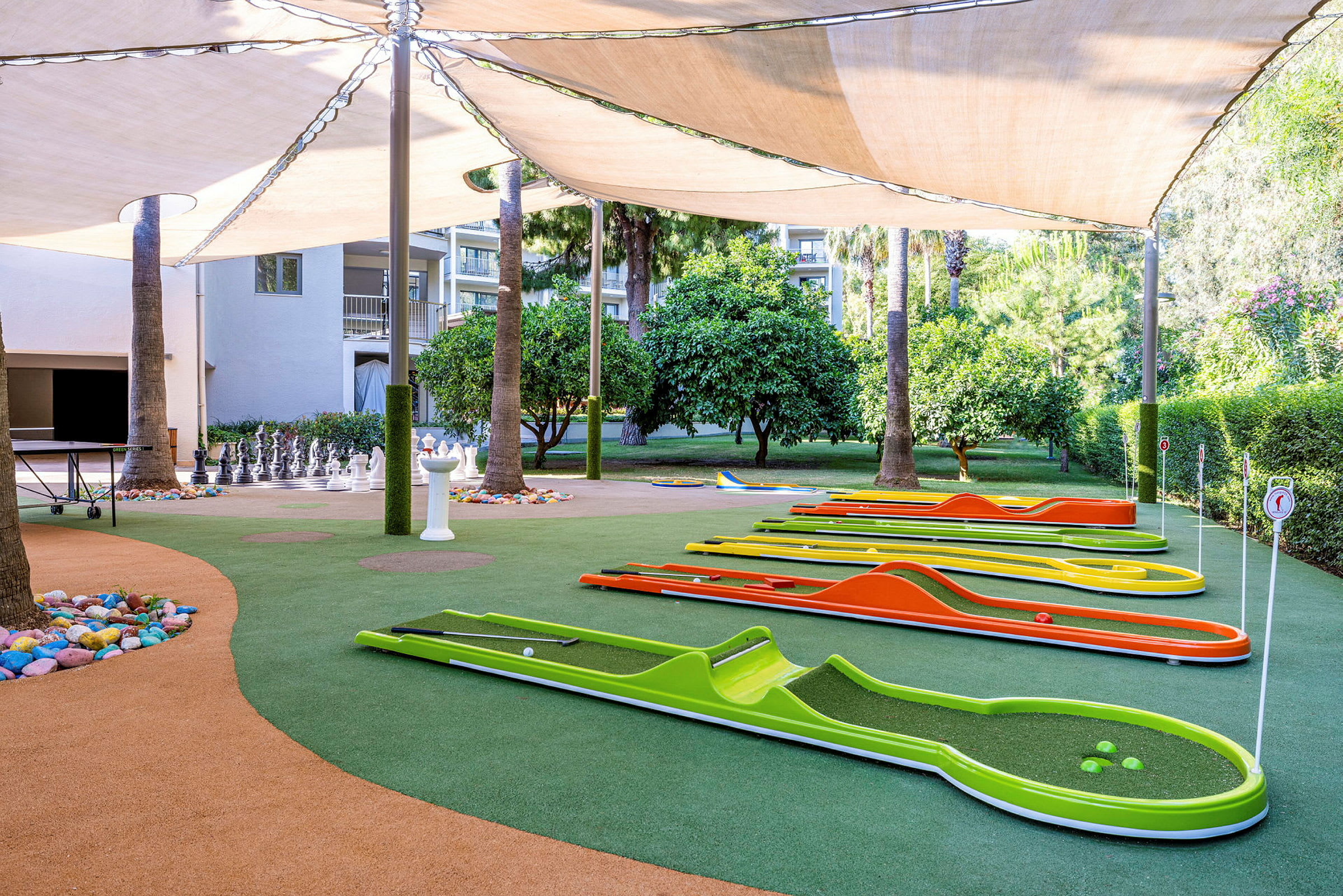 Minigolf-rata, jossa värikkäitä ratoja ja shakkipelejä varjojen alla. (Tekoälyn luoma teksti)