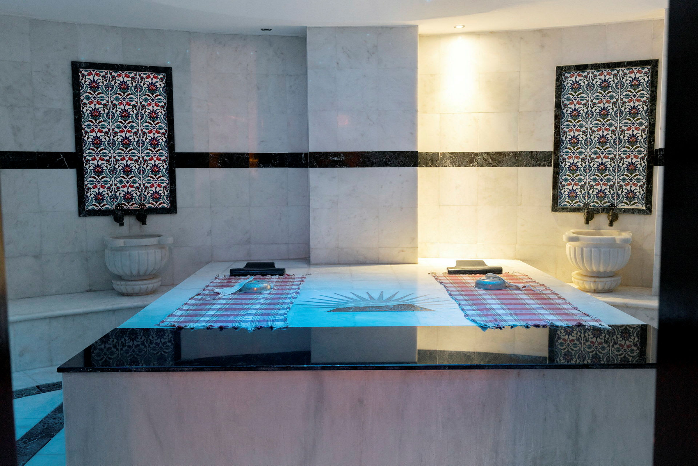 Hamam-huone, jossa marmorialustoja, koristeellisia seinäpaneeleja ja käsienpesualtaita. (Tekoälyn luoma teksti)