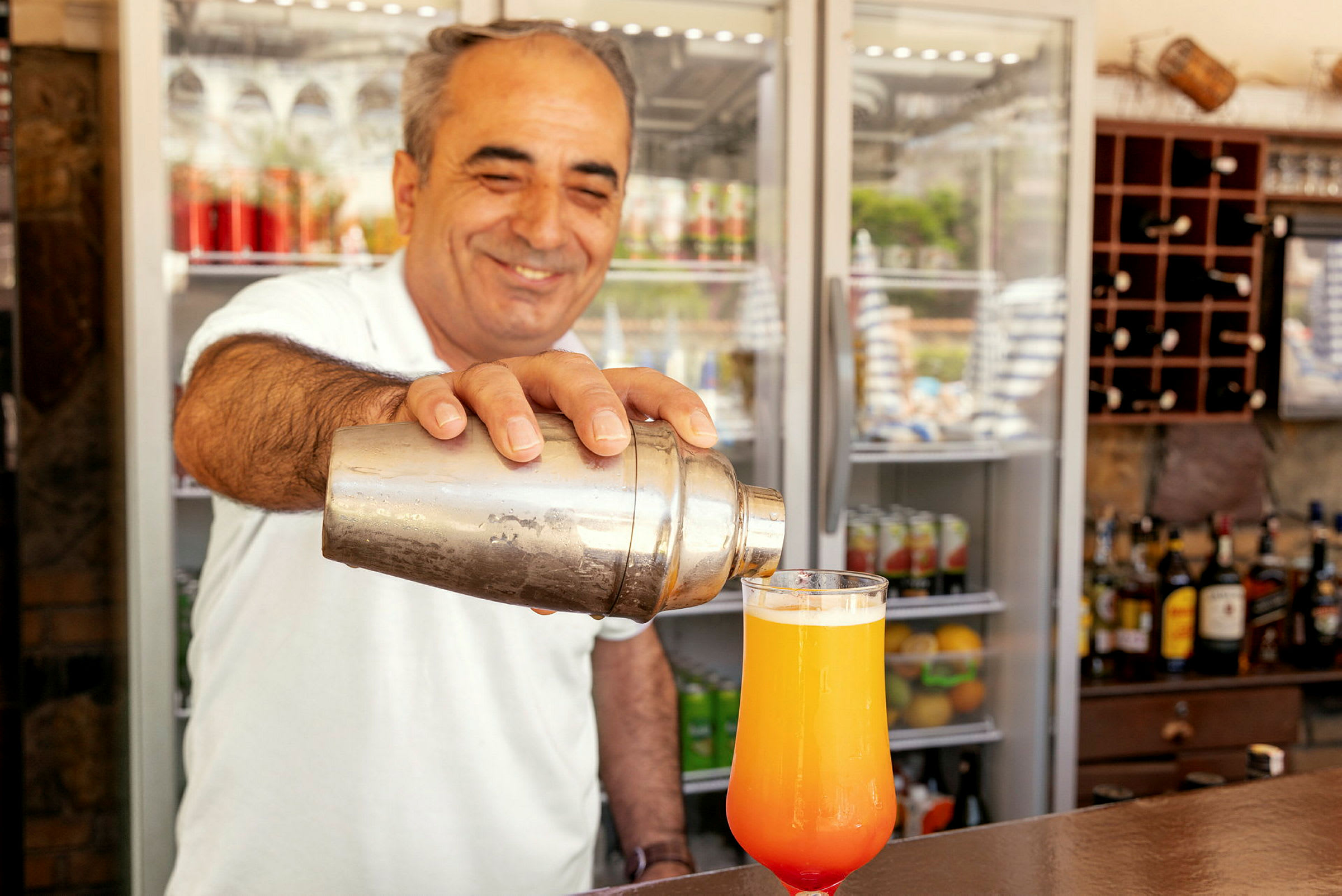 Henkilö pitää cocktail-shakeria ja kaataa juomaa lasiin. (Tekoälyn luoma teksti)