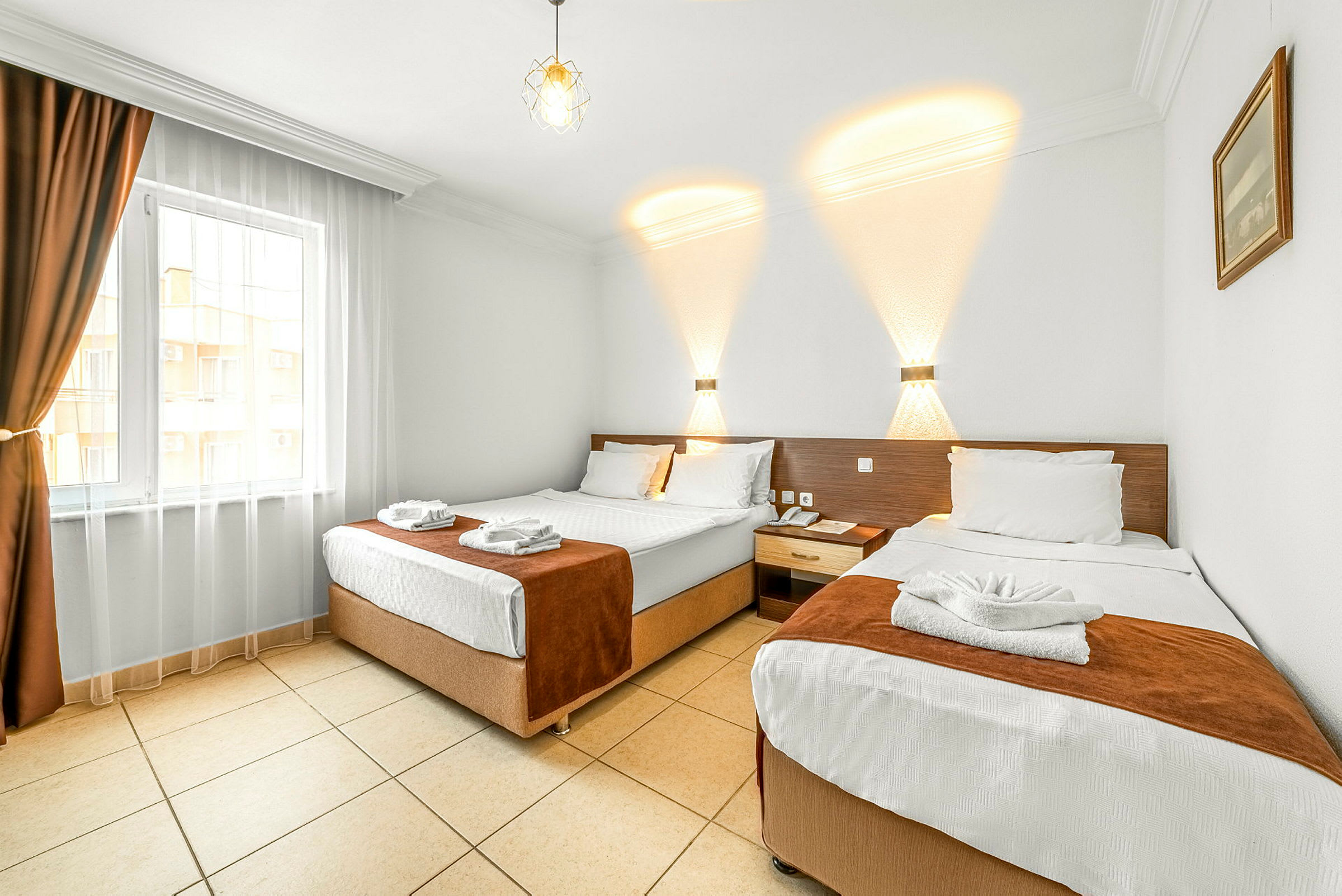 Hotellihuone, jossa on kaksi erillistä sänkyä, vaalea sisustus ja ikkuna, jossa on tummat verhot. (Tekoälyn luoma teksti)
