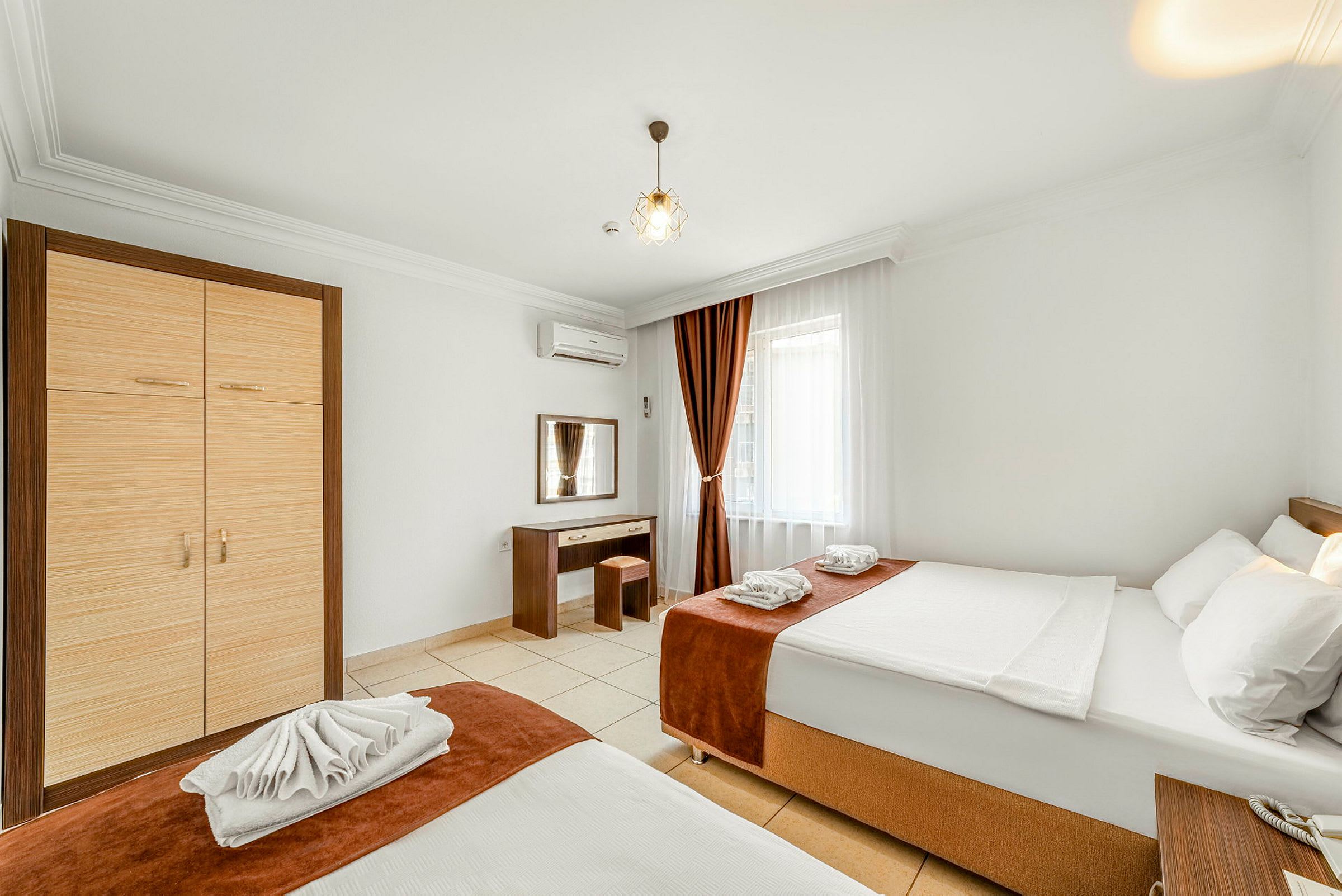 Hotellihuone, jossa on kaksi sänkyä, vaatekaappi, työpöytä ja ikkuna verhoilla. (Tekoälyn luoma teksti)