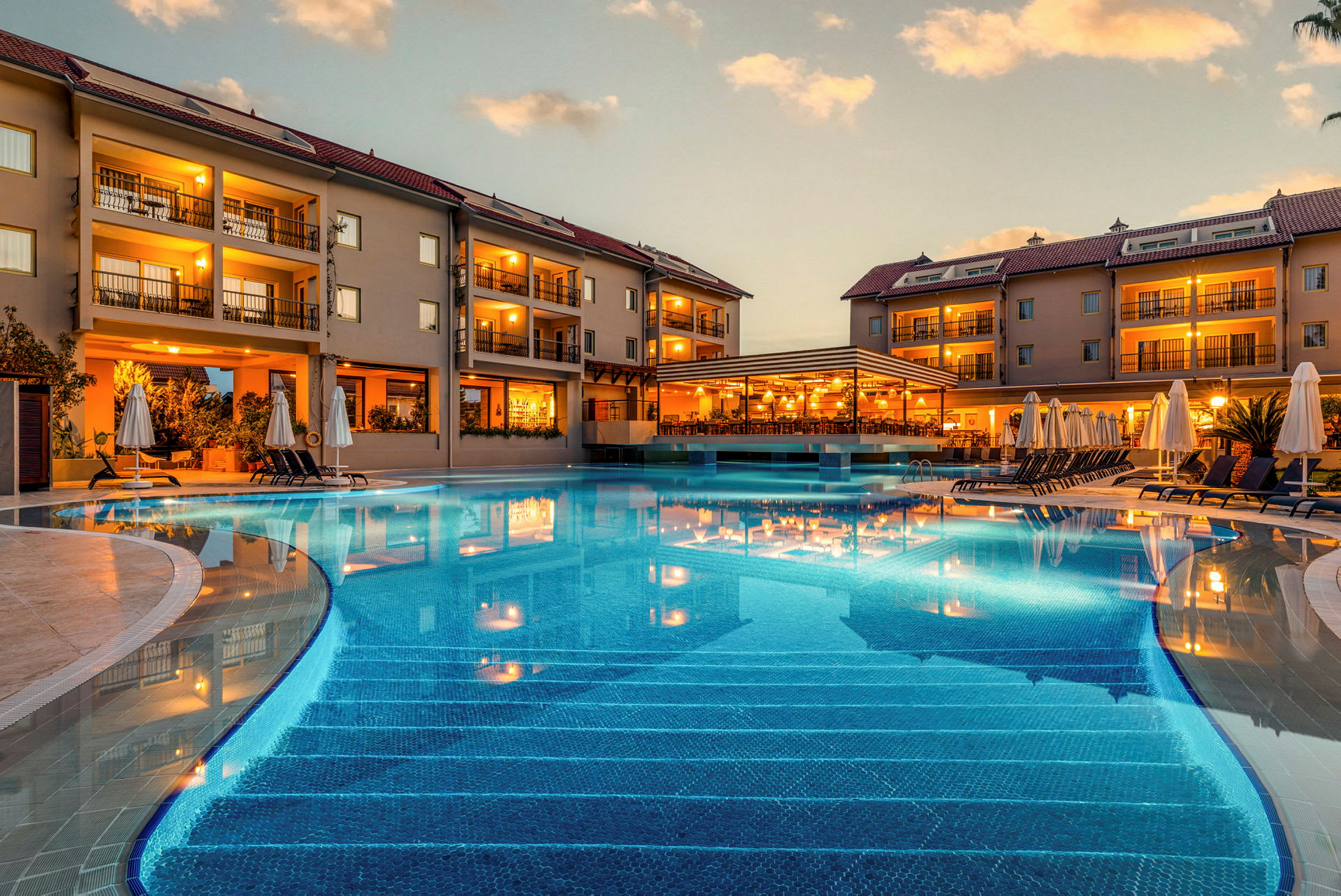 Hotellikompleksi uima-altaineen ja aurinkotuoleineen hämärän aikaan. (Tekoälyn luoma teksti)