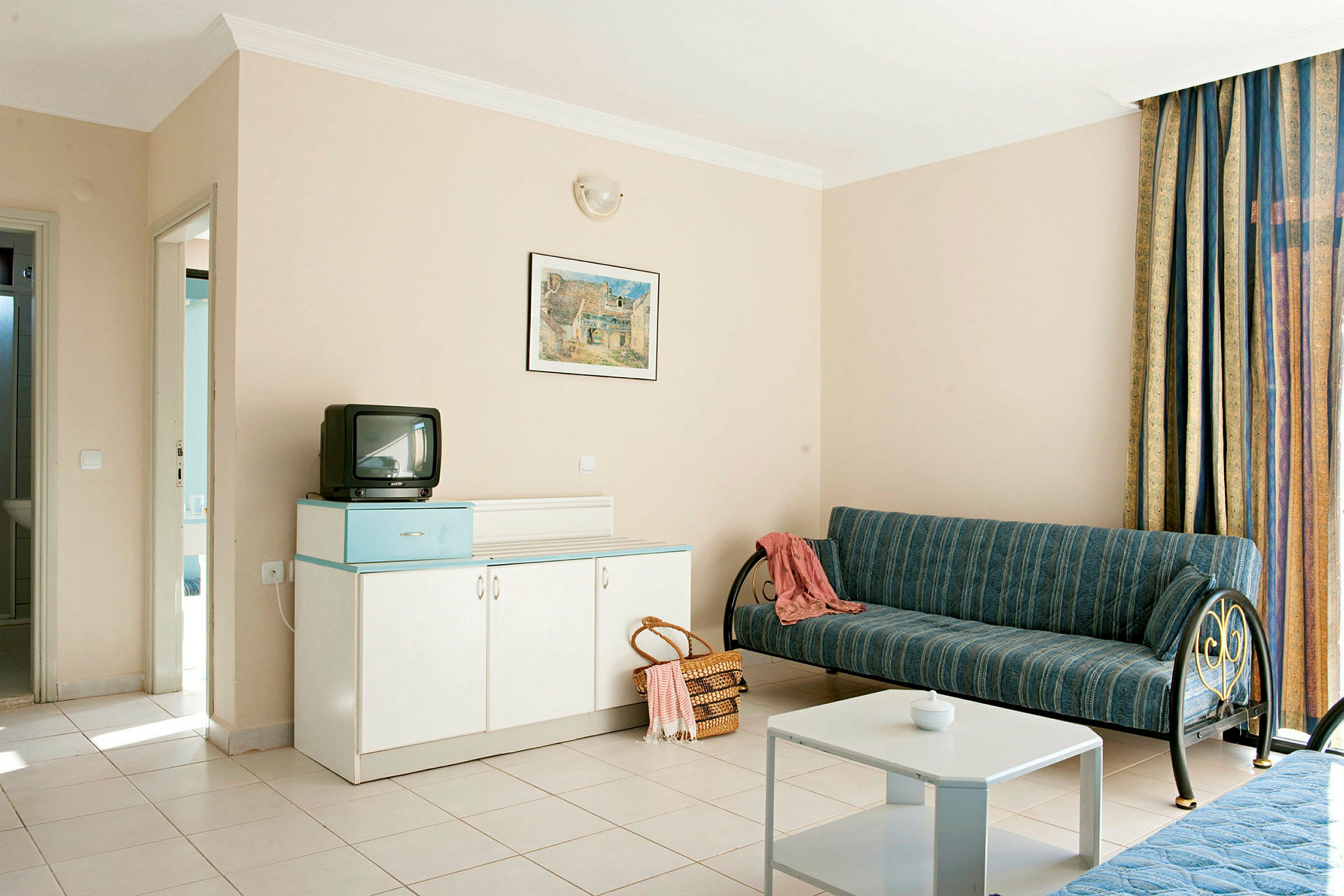 Hotellihuone, jossa sohva, pöytä, kaappi ja pieni televisio. (Tekoälyn luoma teksti)