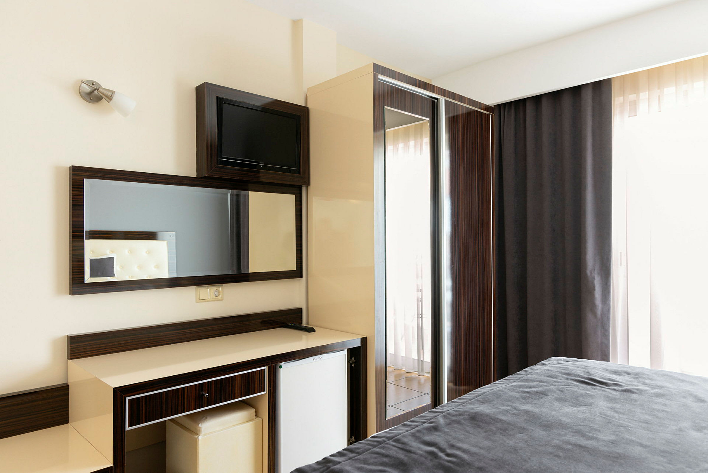 Hotellihuone, jossa on kirjoituspöytä, peili ja jääkaappi. (Tekoälyn luoma teksti)