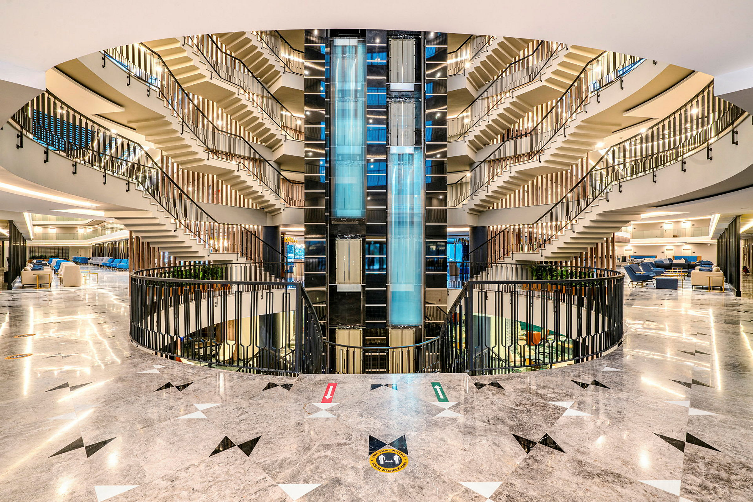 Hotellin atrium, jossa valaistussuunnittelua, lasisia hissejä ja ylöspäin johtavia portaita. (Tekoälyn luoma teksti)