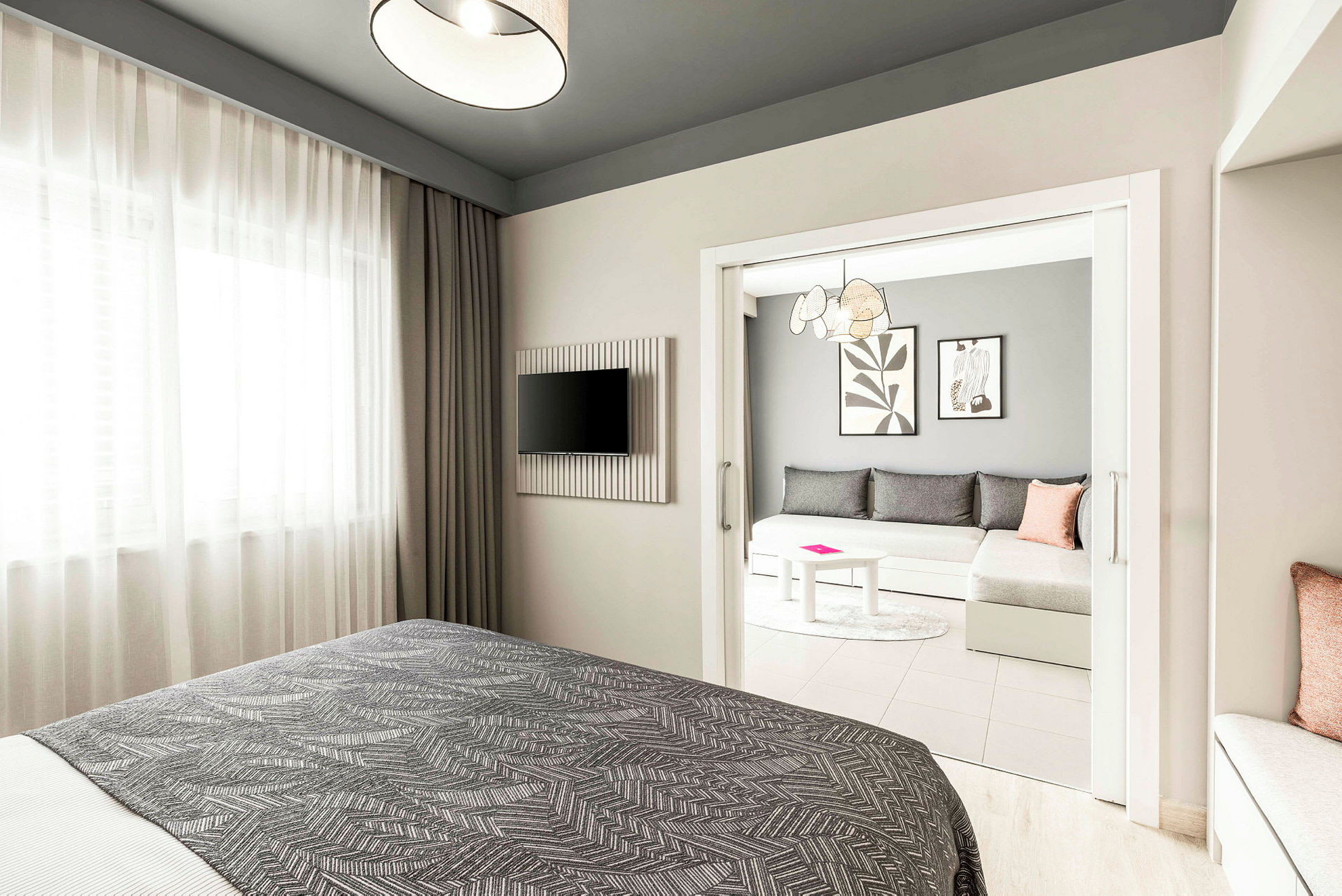 Hotellihuone, jossa etualalla sänky, seinällä televisio ja erillinen istuinryhmä, jossa sohva ja pöytä. (Tekoälyn luoma teksti)