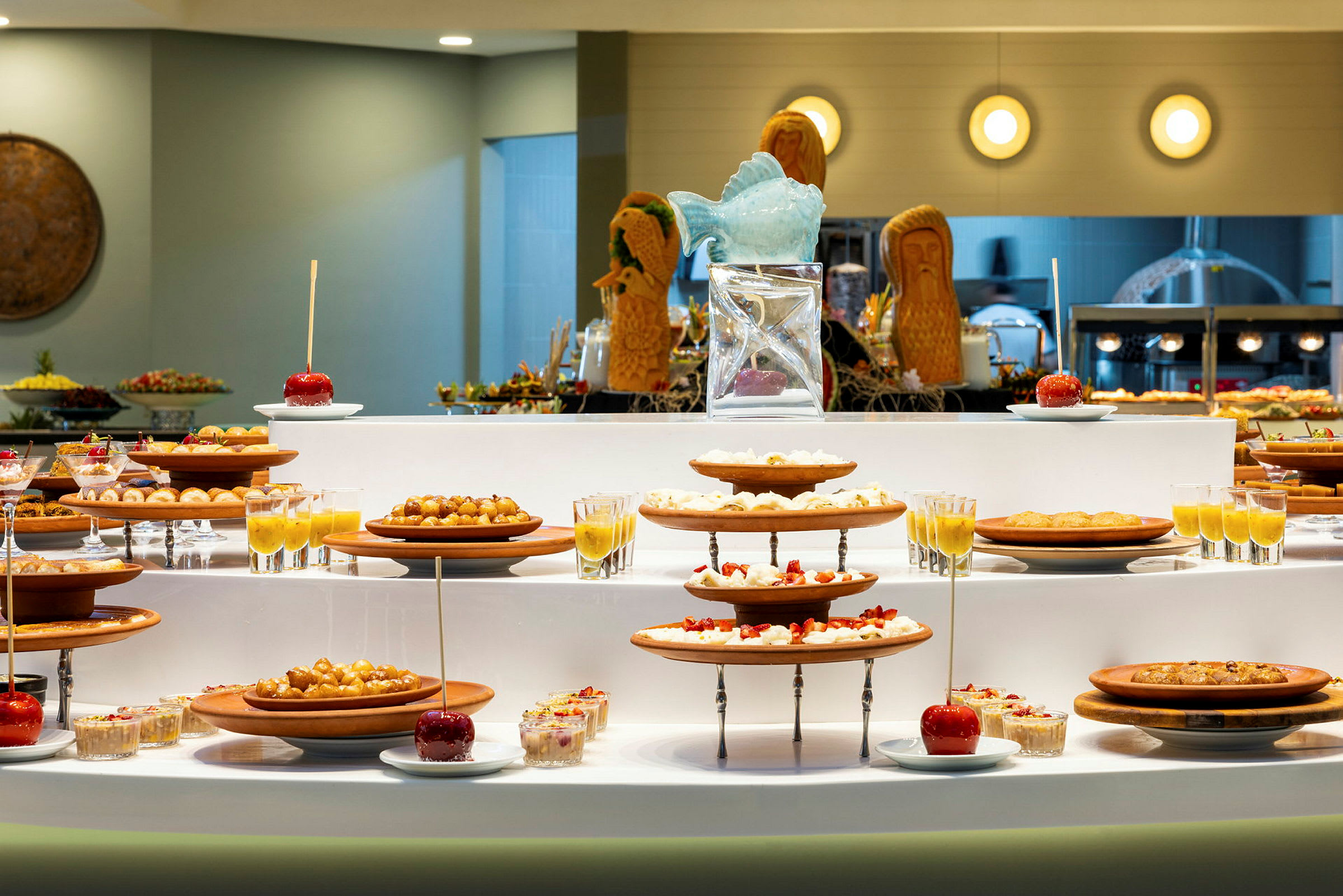 Buffet, joka sisältää erilaisia jälkiruokia ja hedelmiä tarjottimilla ja laseilla. (Tekoälyn luoma teksti)