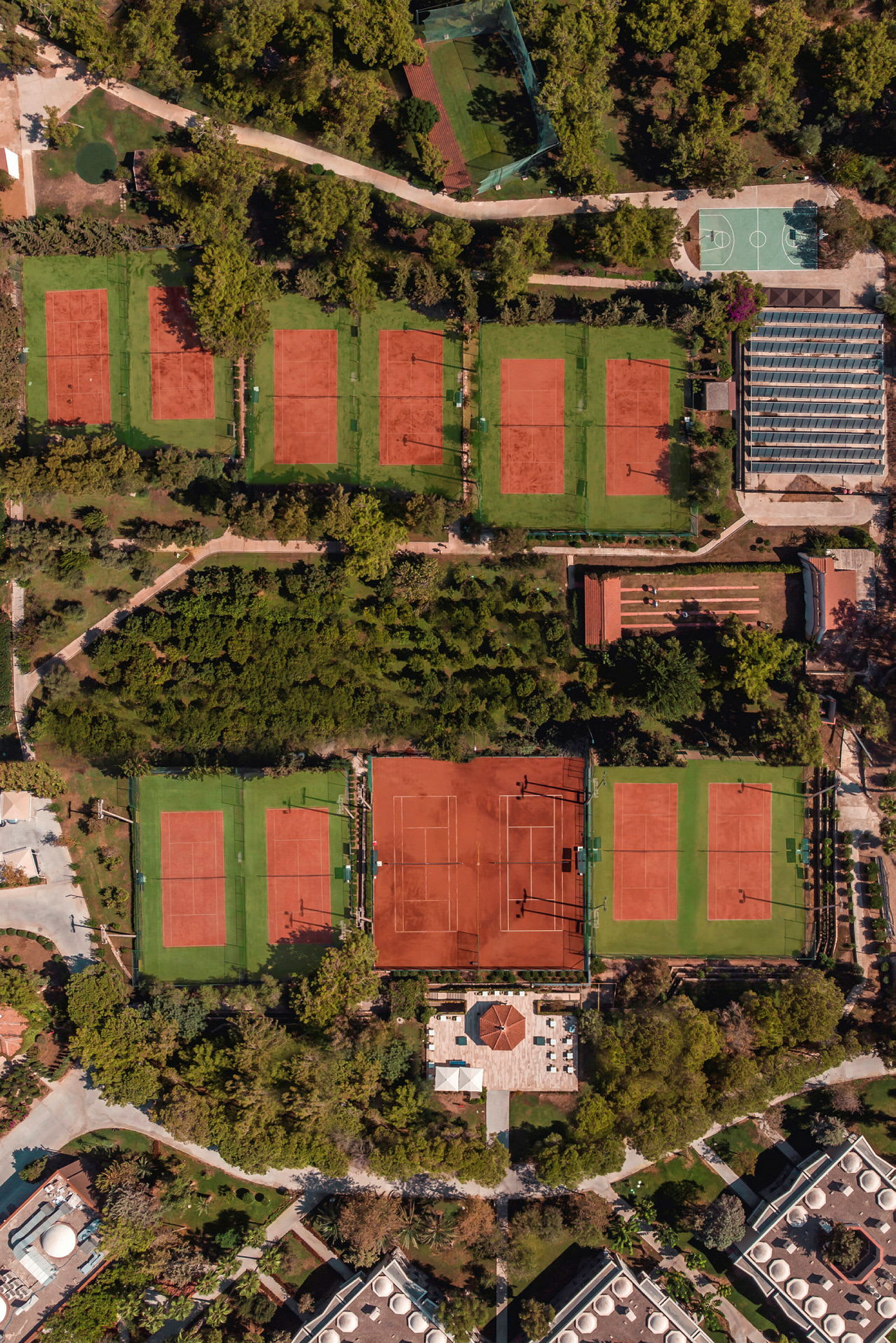 Kuva useista punahiekkapintaisista tennisalueista, joita ympäröi vihreä kasvillisuus. (Tekoälyn luoma teksti)