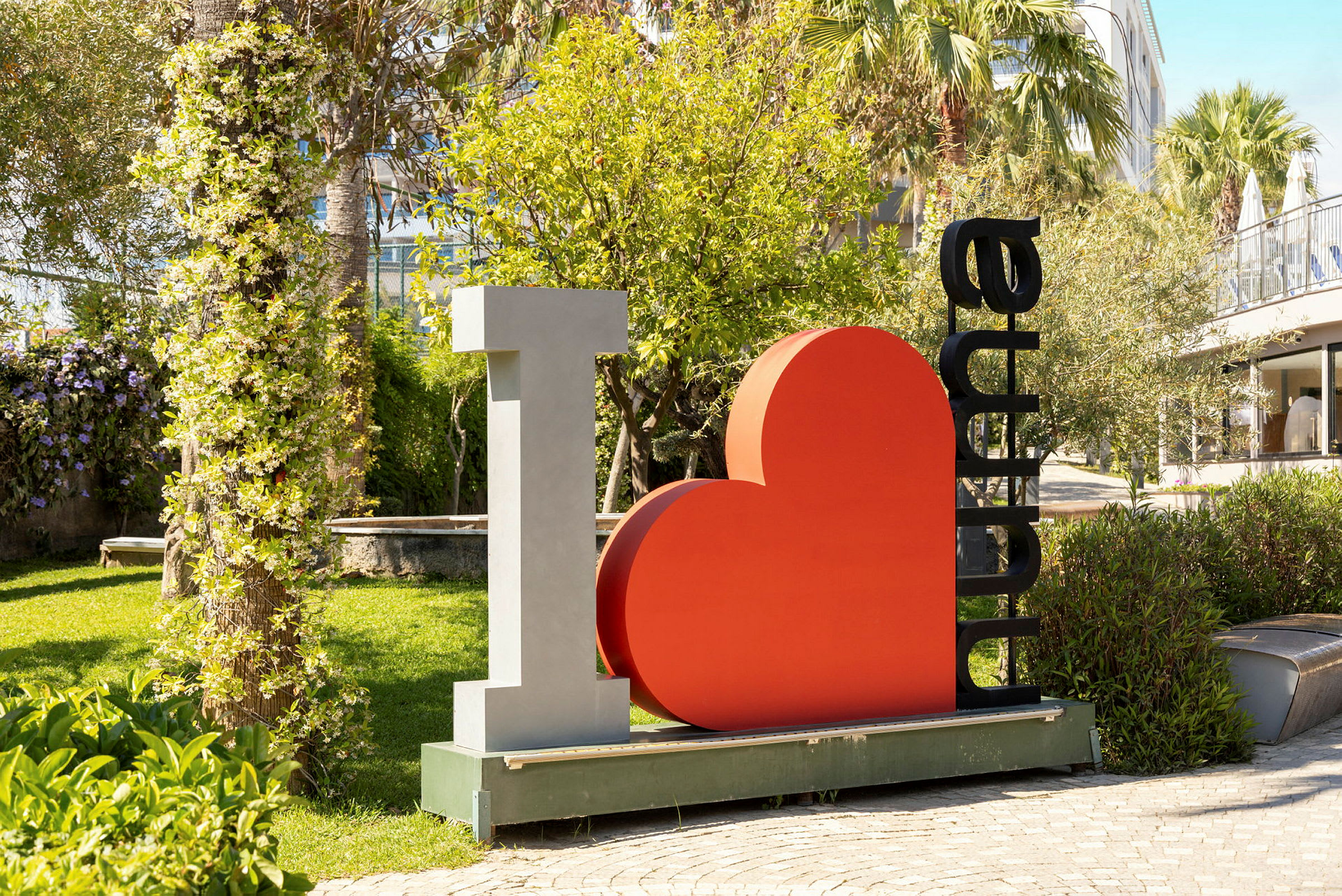 Veistoksessa on teksti "I ♡ Alanya" ja sitä ympäröi vehreä puutarha. (Tekoälyn luoma teksti)
