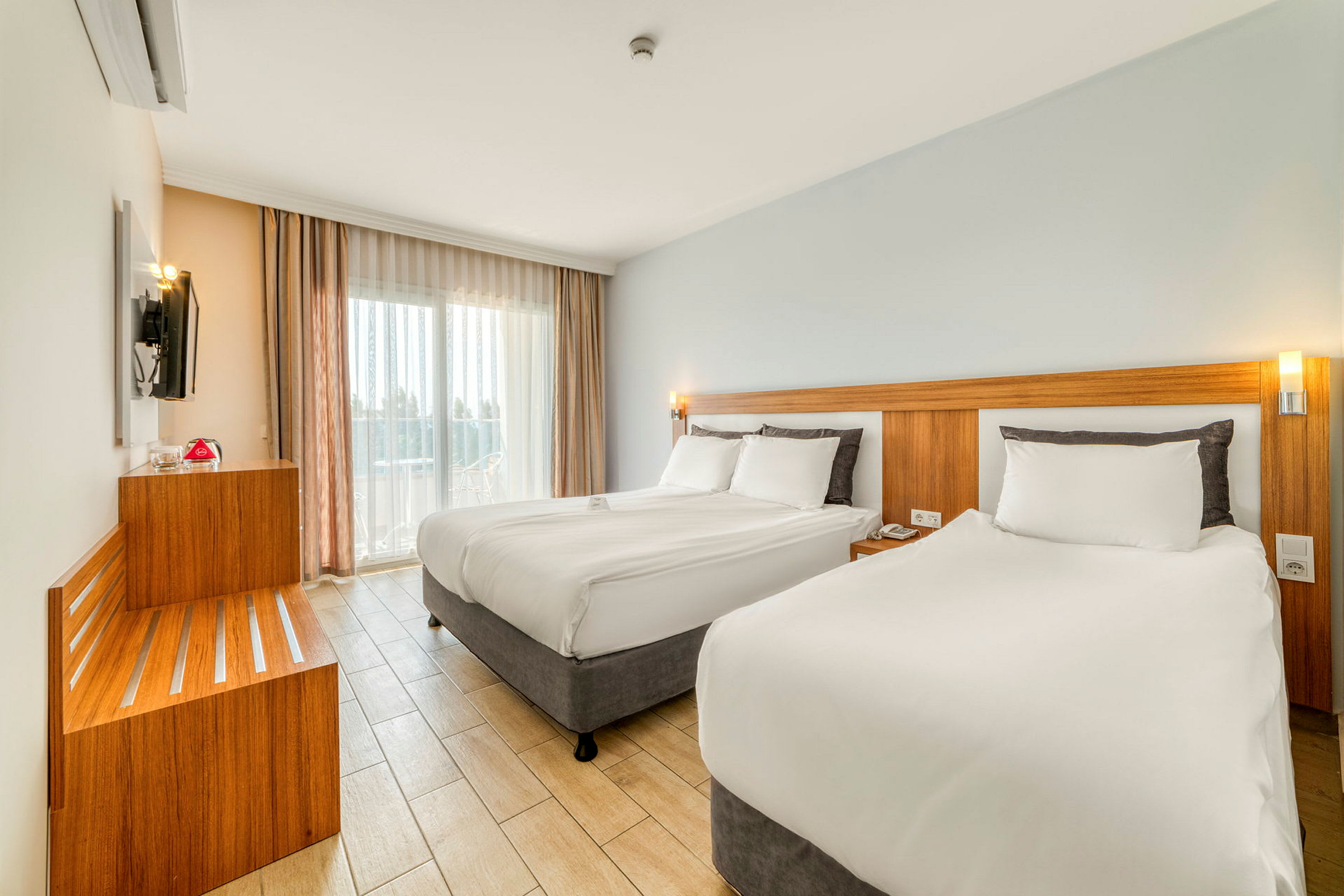 Moderni hotellihuone, jossa on kaksi sänkyä, vaaleat värit ja suuret ikkunat. (Tekoälyn luoma teksti)