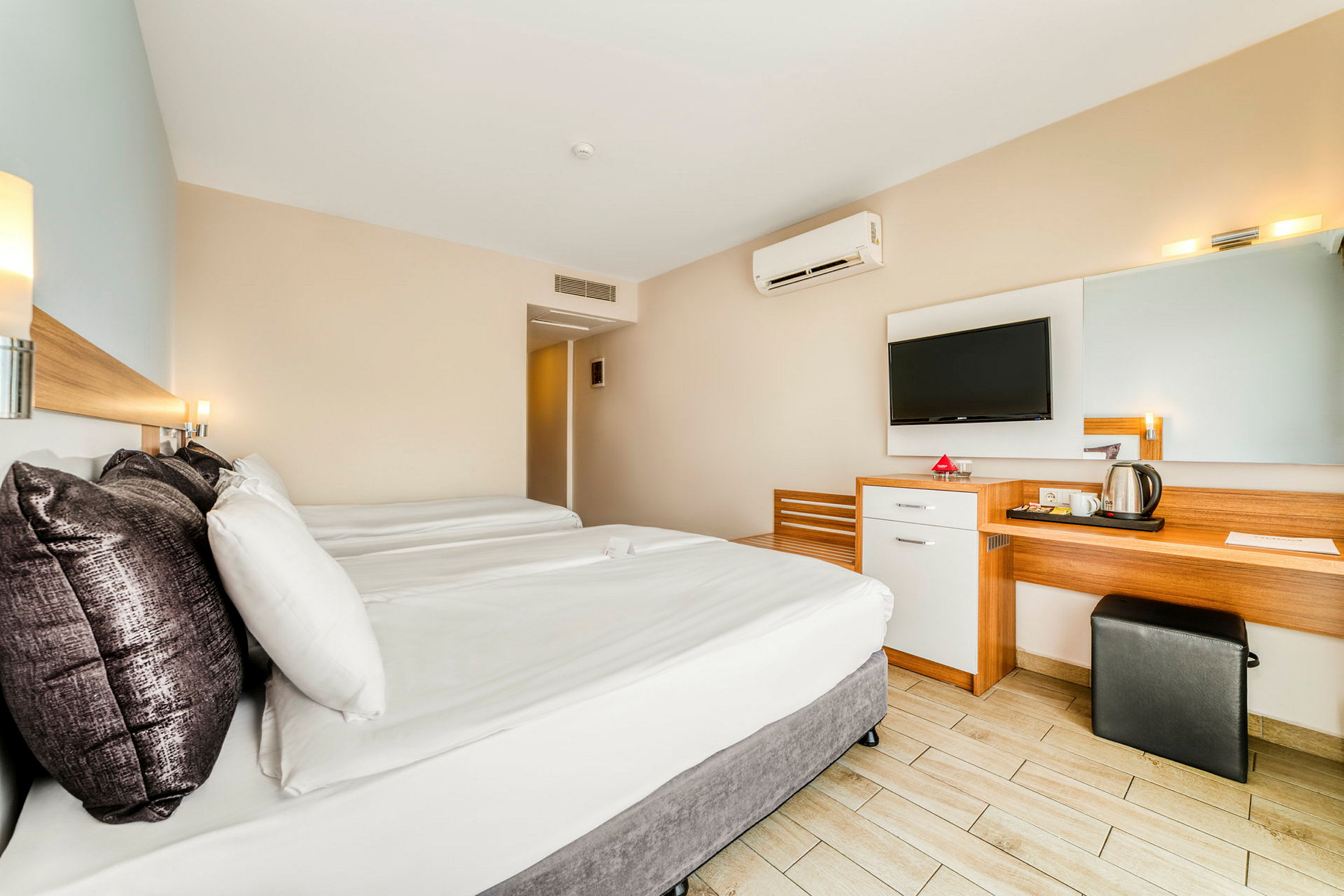 Hotellihuone, jossa on kaksi sänkyä, työpöytä, peili ja seinään kiinnitetty TV. (Tekoälyn luoma teksti)