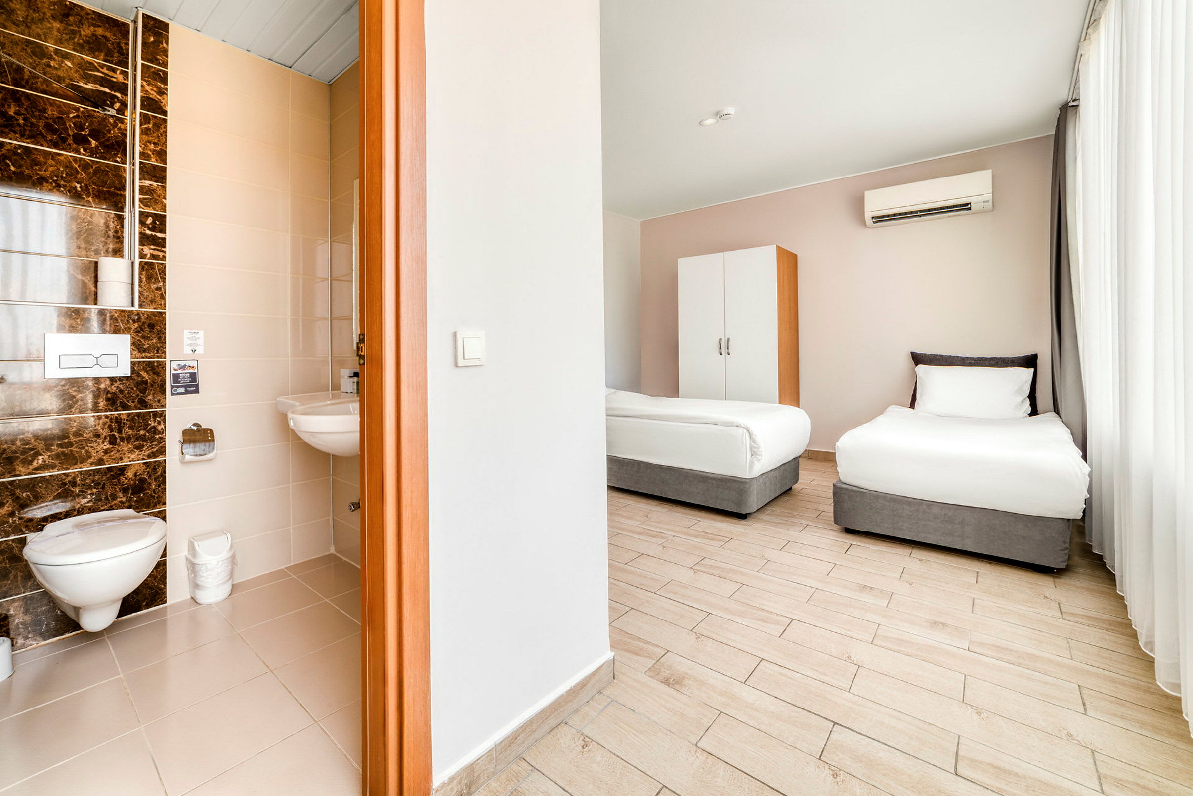 Hotellihuone, jossa kaksi yhden hengen vuodetta ja osittain näkyvissä keittiö ja kylpyhuone. (Tekoälyn luoma teksti)
