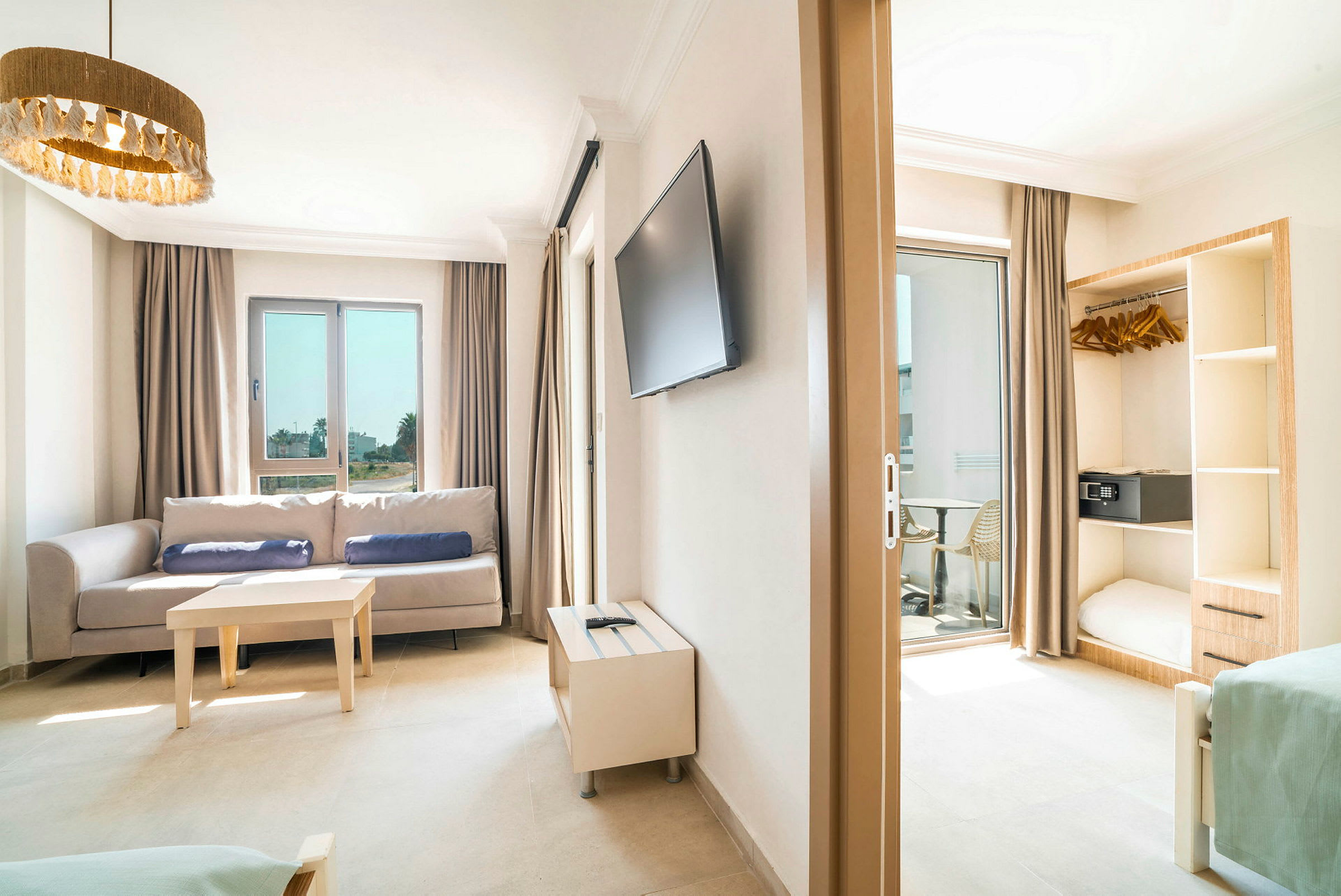 Kuva vaaleasta hotellihuoneesta, jossa on sohva, pöytä, televisio ja avoin vaatekaappi. (Tekoälyn luoma teksti)